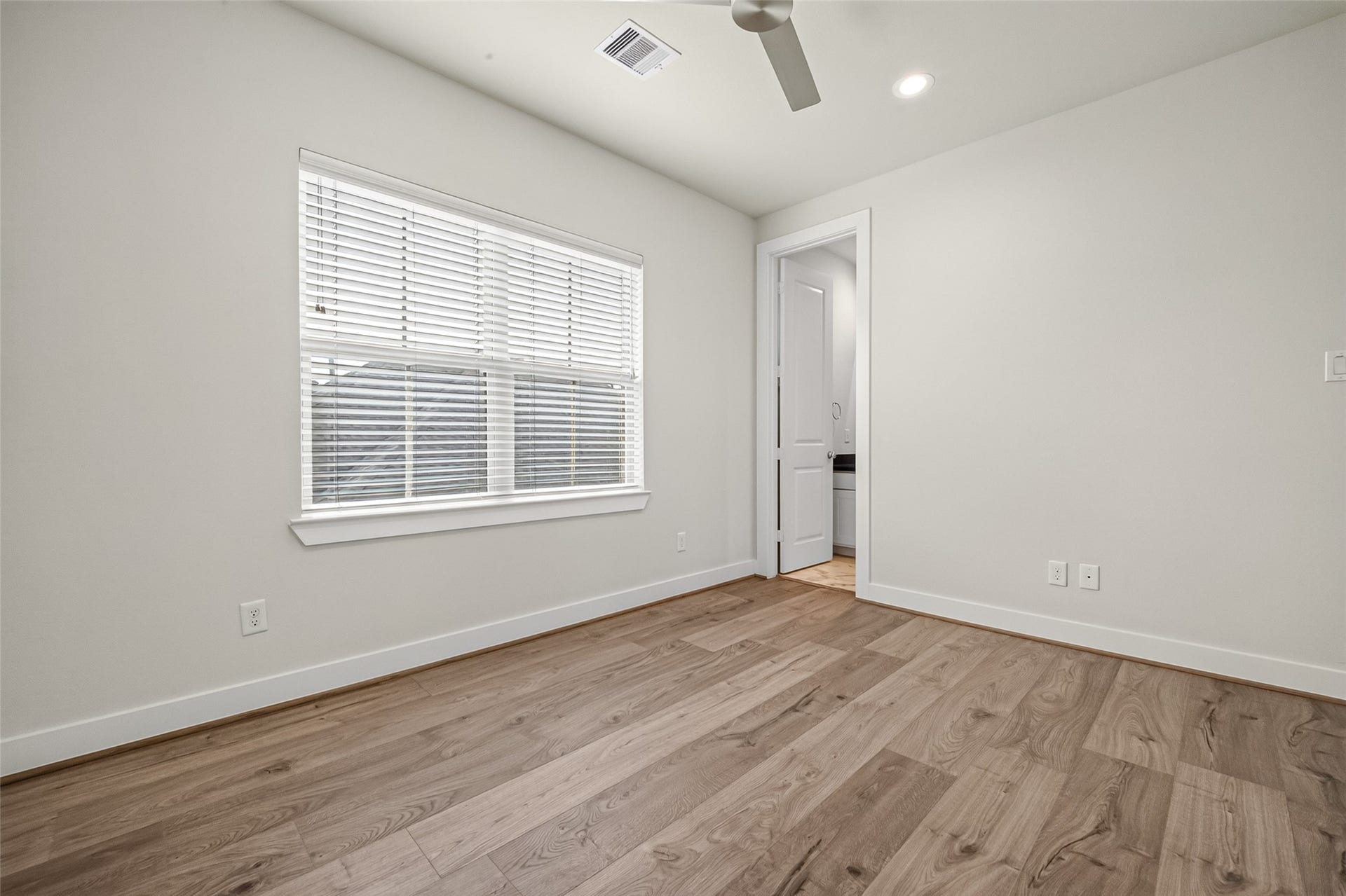 Bright bedroom featuring sleek floors, a large window for natural light, and an adjoining door leading to a bathroom.