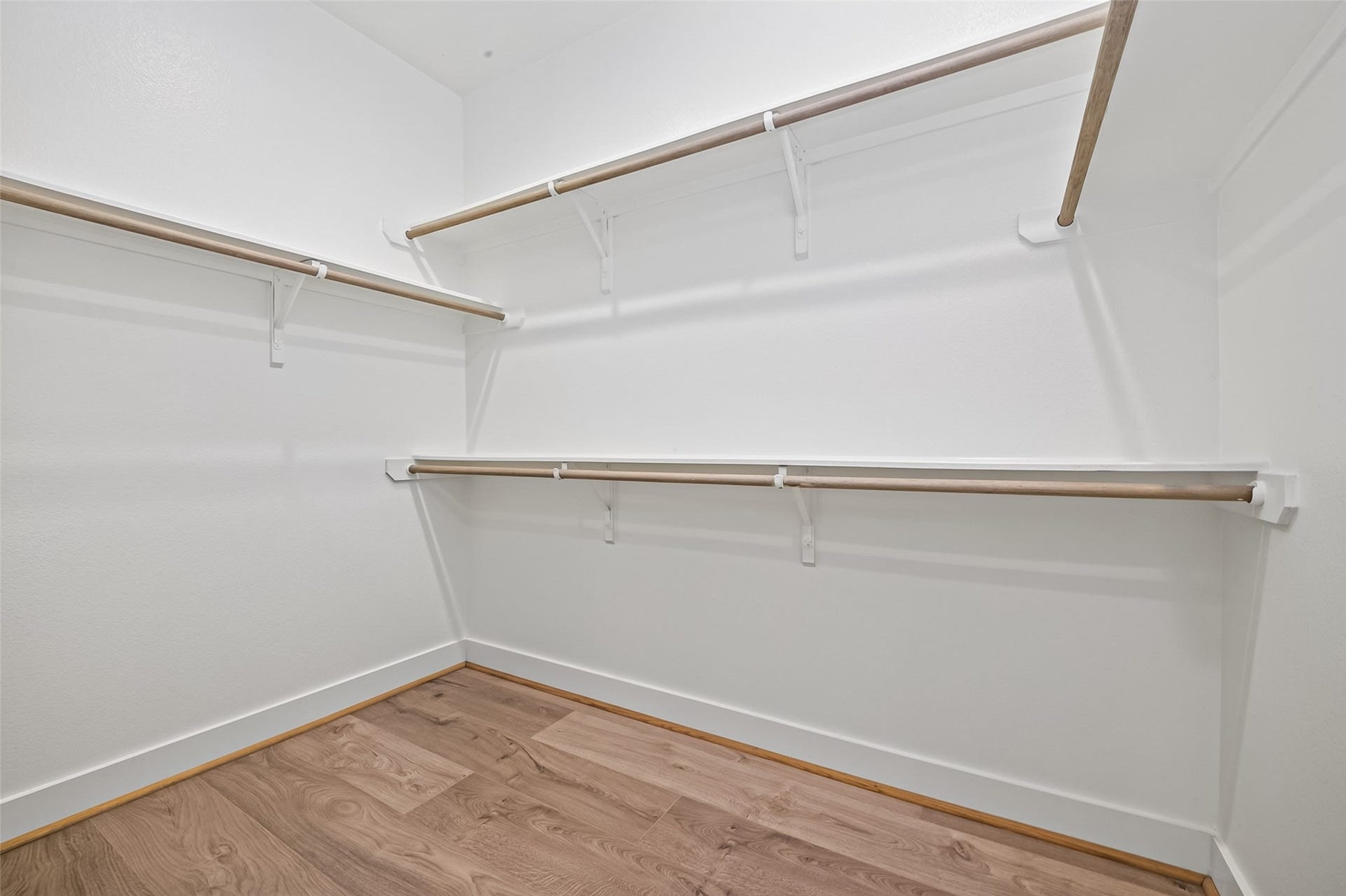 Spacious walk-in closet with ample shelving and hanging space, featuring sleek LVP floors and bright white walls for a modern touch.