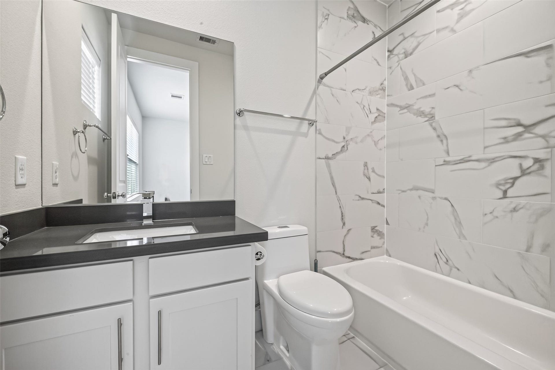 Sleek bathroom with elegant marble-patterned tiles, a modern vanity with a polished countertop, and a pristine bathtub for a luxurious touch.
