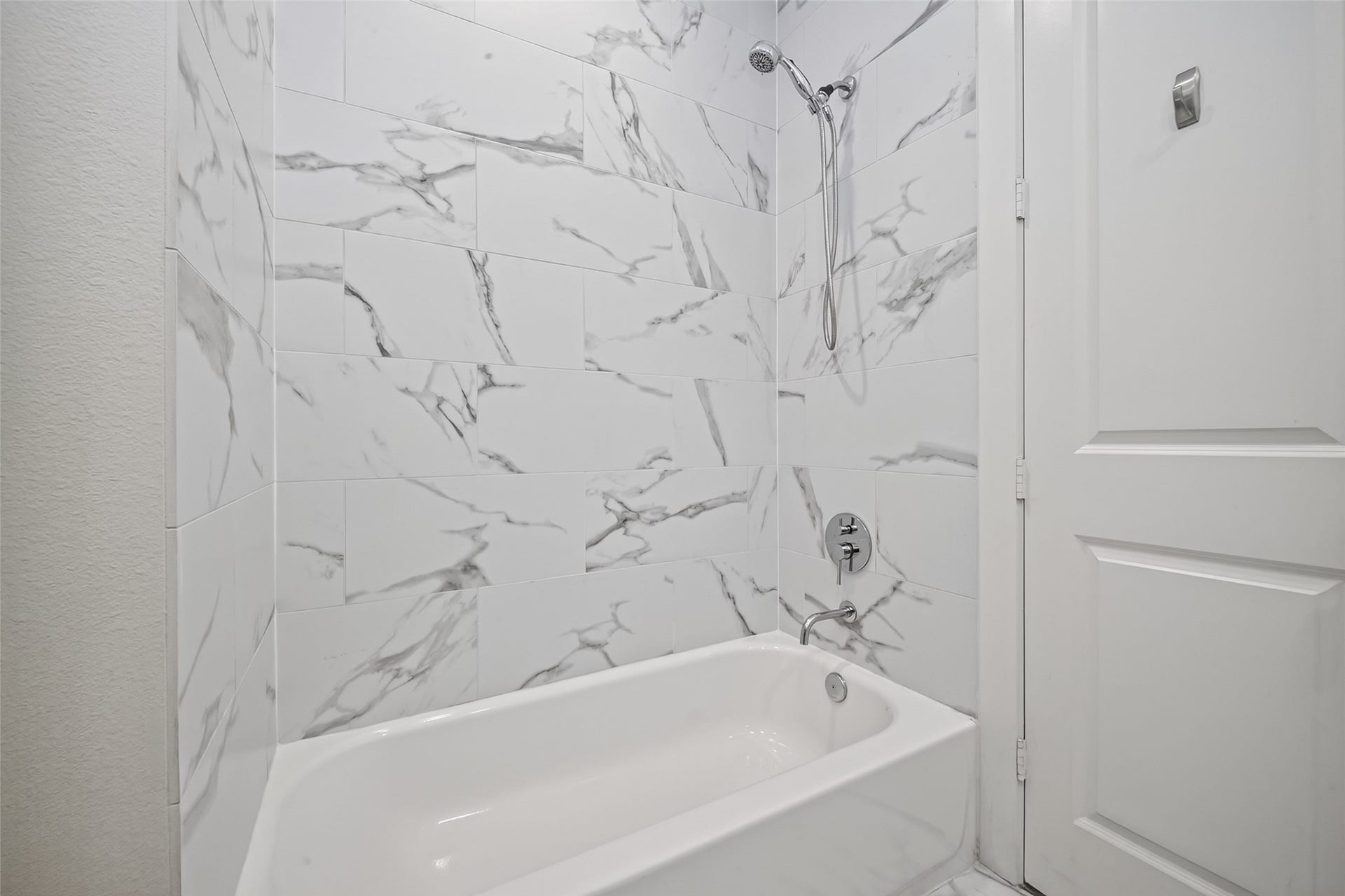 Elegant bathroom featuring a modern bathtub with sleek marble-patterned tiles and a polished chrome shower fixture.