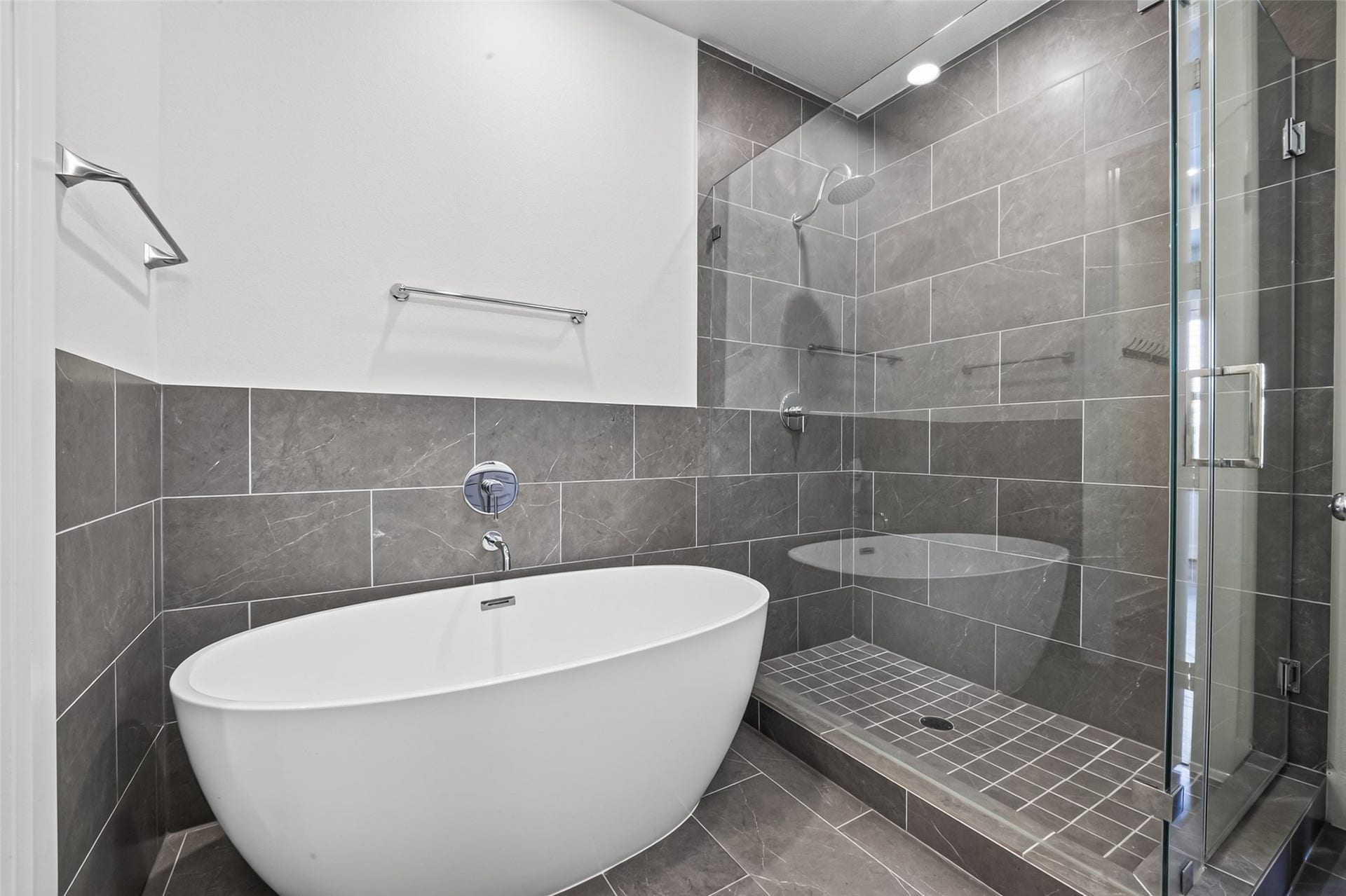 Luxurious bathroom featuring a sleek freestanding tub and a modern glass-enclosed shower with elegant gray tilework.