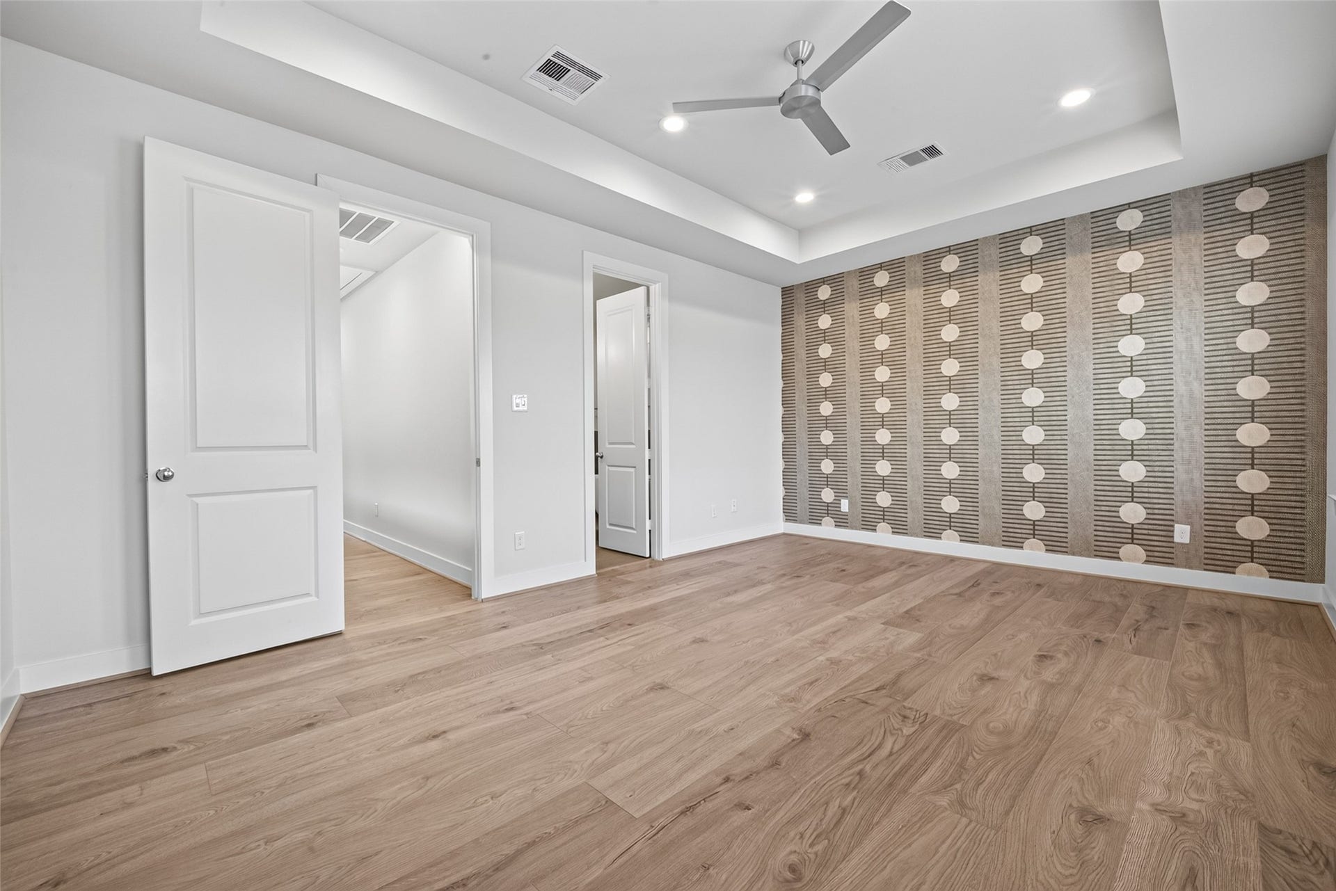 Spacious Master Suite bedroom featuring elegant wood like flooring, a unique accent wall, and a modern ceiling fan, complemented by recessed lighting and ample closet space.