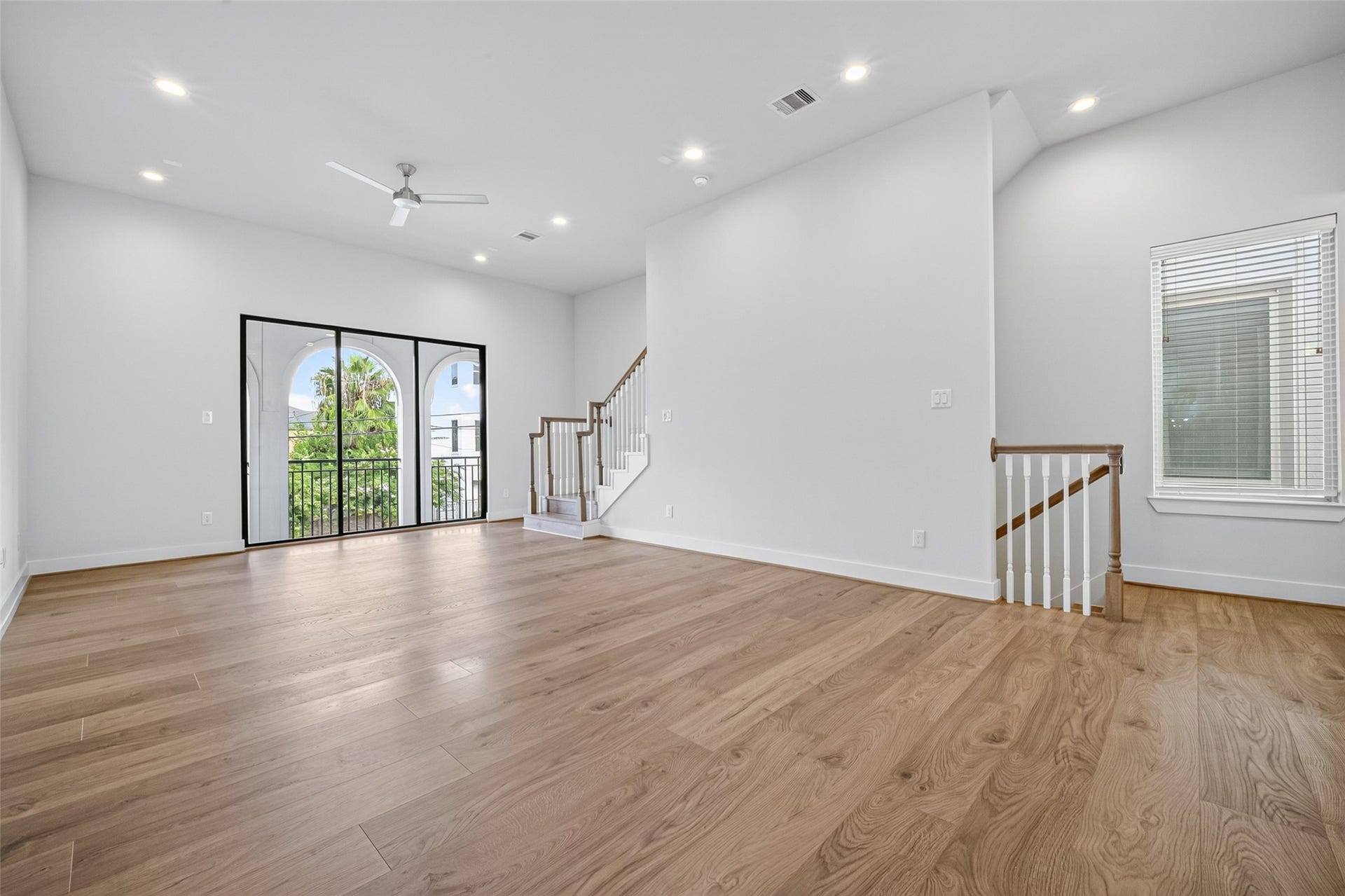 Spacious and bright living area featuring elegant Swiss floors, recessed lighting, and large windows with sliding doors leading to a charming balcony.