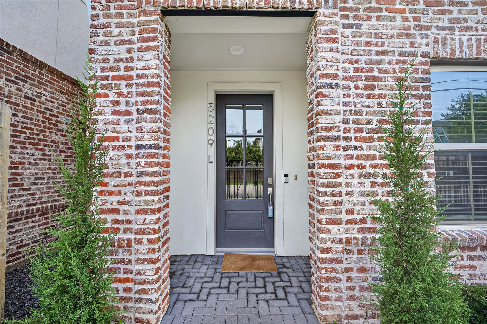 Charming brick and Stucco entryway and enclosed fenced yard with a sleek, modern door and elegant landscaping, creating a warm welcome.