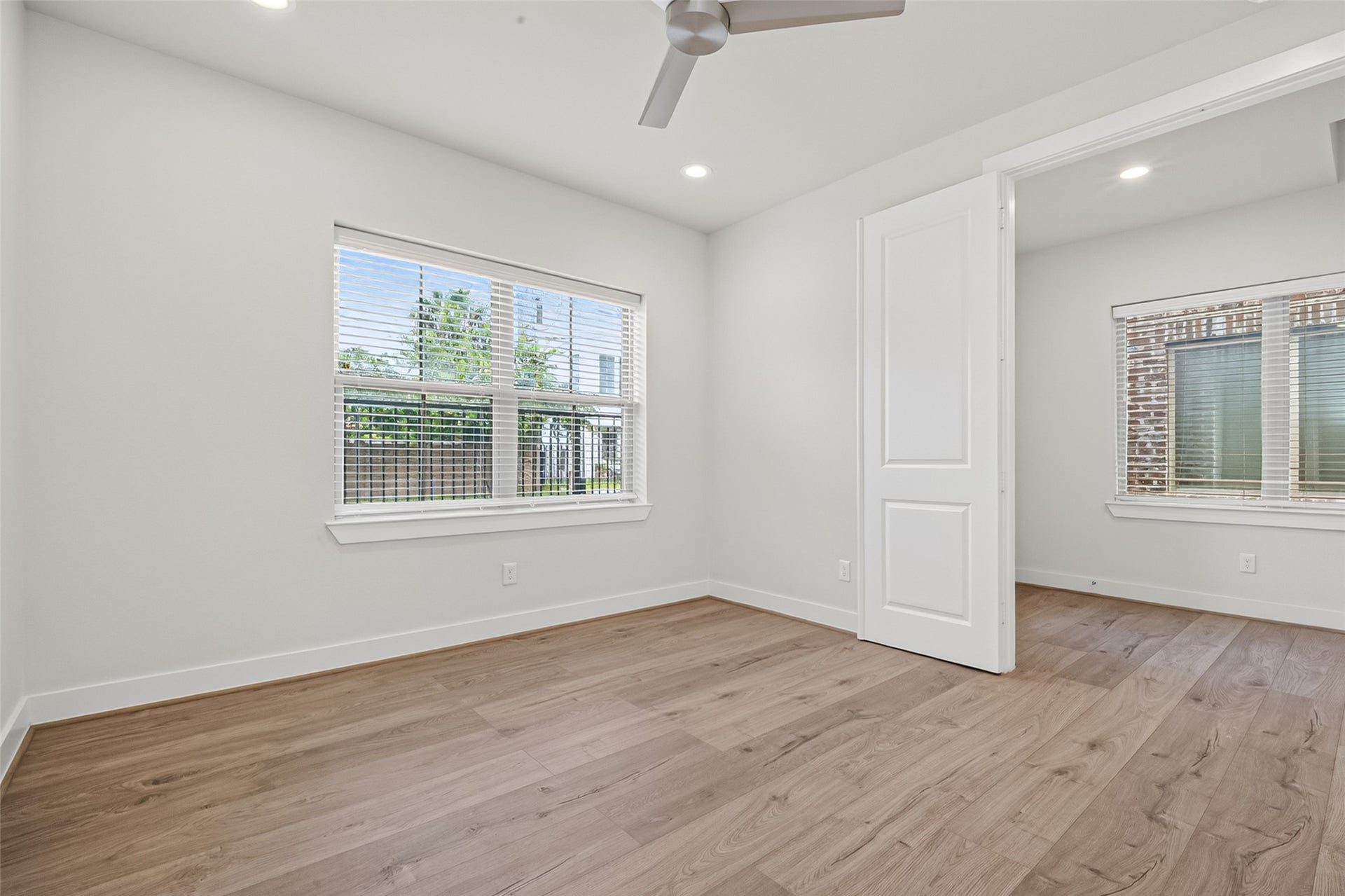 Bright and airy room featuring elegant Swiss flooring, large windows with blinds for ample natural light, and a modern ceiling fan for comfort.