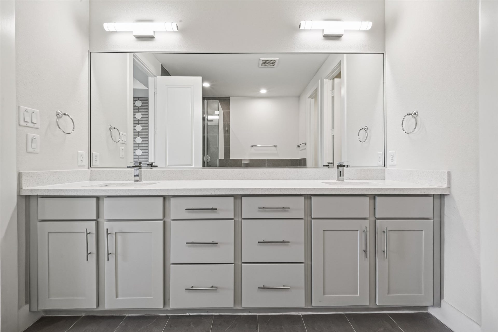 Elegant bathroom featuring a spacious double vanity with sleek gray cabinets, ample storage, and modern lighting, creating a bright and functional space.