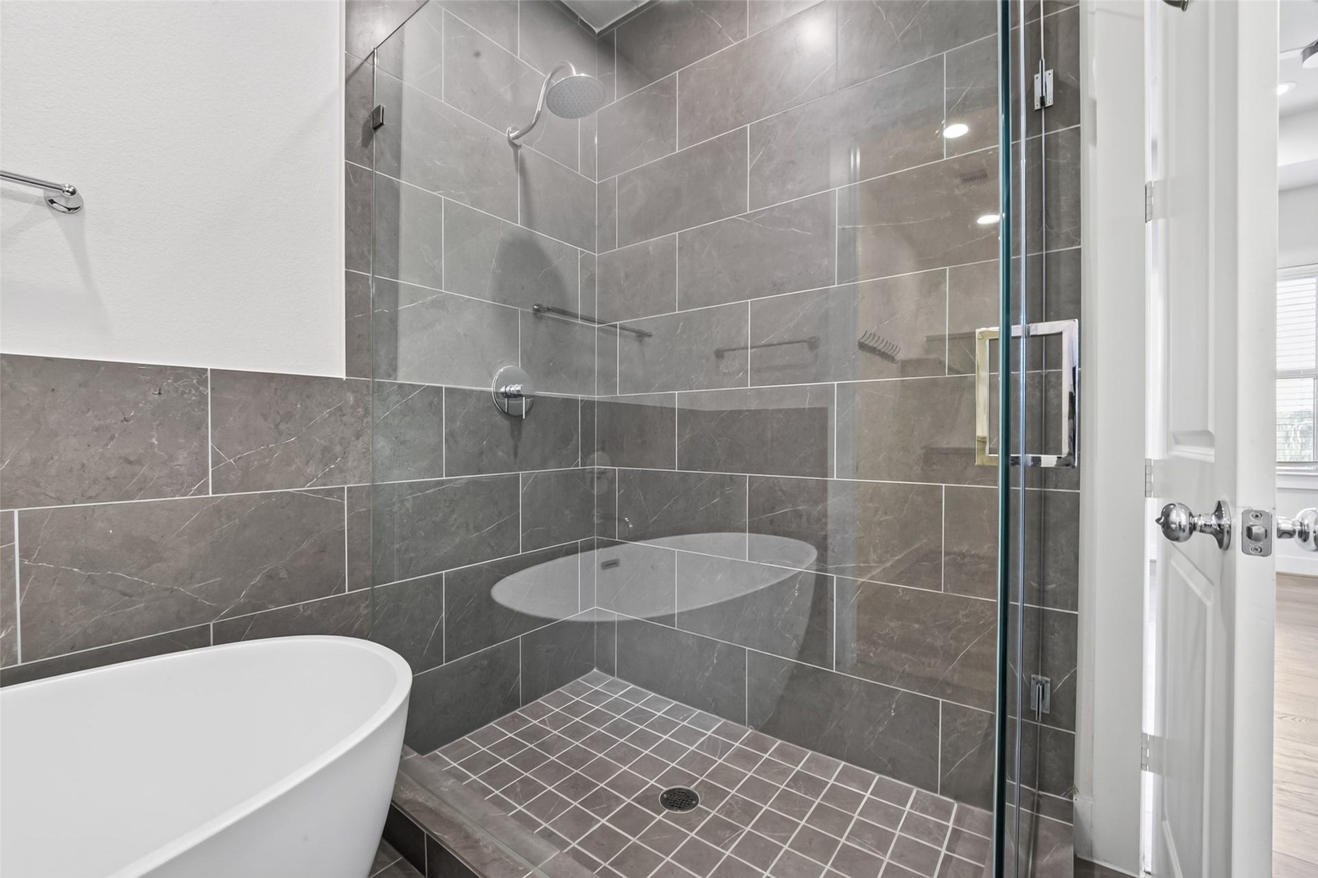 Elegant bathroom featuring a spacious glass-enclosed shower with modern gray tile and a luxurious freestanding bathtub.