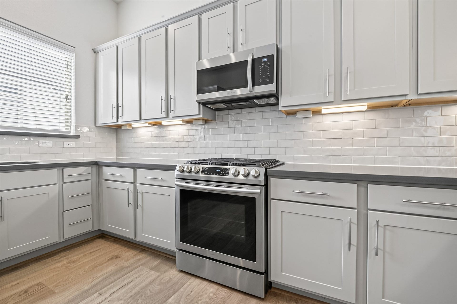 2nd Floor Features a spacious Modern kitchen featuring sleek gray cabinetry, stainless steel appliances, and elegant subway tile backsplash, complemented by warm Swiss wood like flooring.