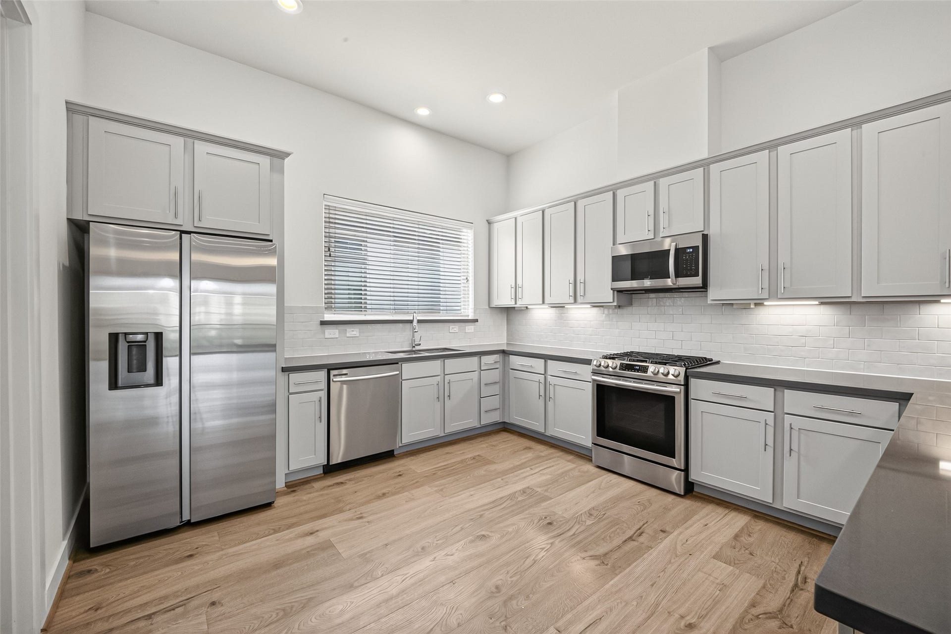Modern kitchen featuring sleek stainless steel appliances, ample cabinetry, and elegant quartz countertops, all complemented by a stylish tile backsplash and warm Swiss floors.