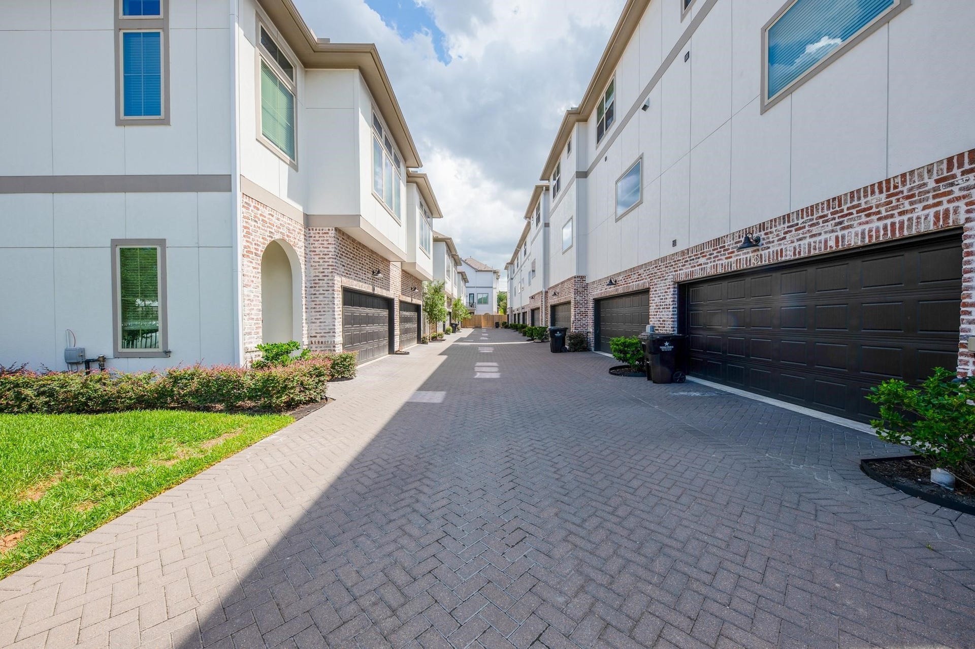 Modern townhome community with dual-level designs, featuring sleek brick and stucco exteriors and spacious two-car garages along a landscaped cobblestone pathway.
