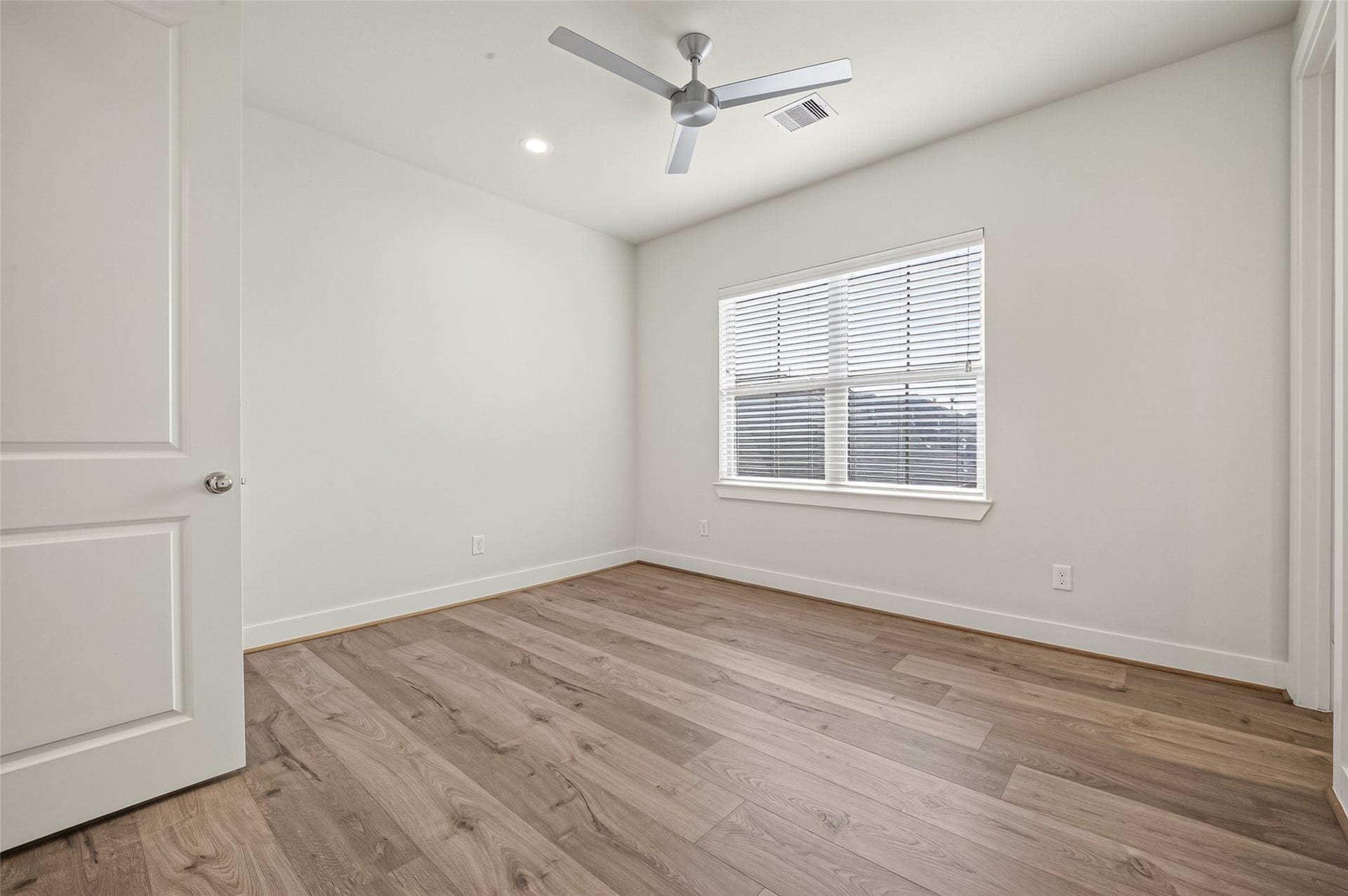 Bright and inviting Secondary beroom featuring elegant wood like flooring, a modern ceiling fan, and ample natural light streaming through a large window with blinds.