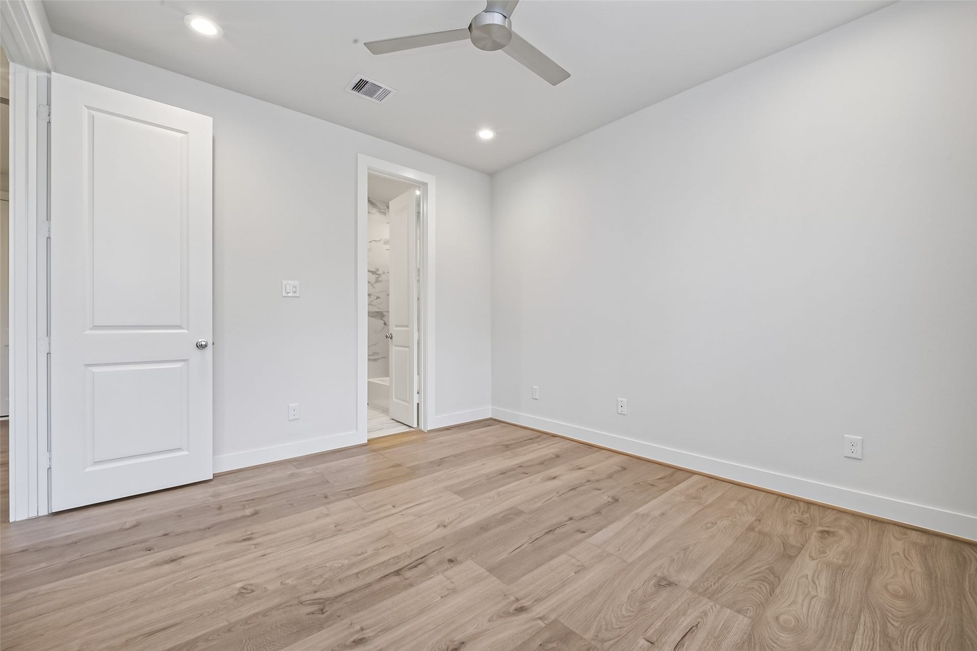 Bright and spacious bedroom / Office featuring sleek Swiss wood like flooring, a ceiling fan, and easy access to the ensuite bathroom through a modern door.