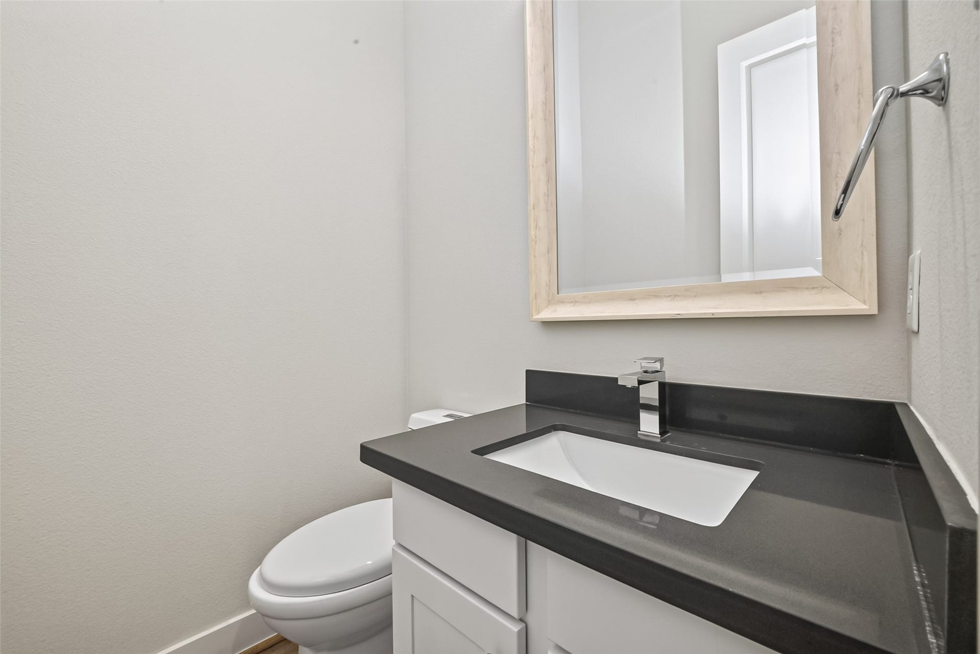 Modern half-bathroom located on main floor featuring a sleek taupe countertop, contemporary faucet, and a stylish framed mirror.