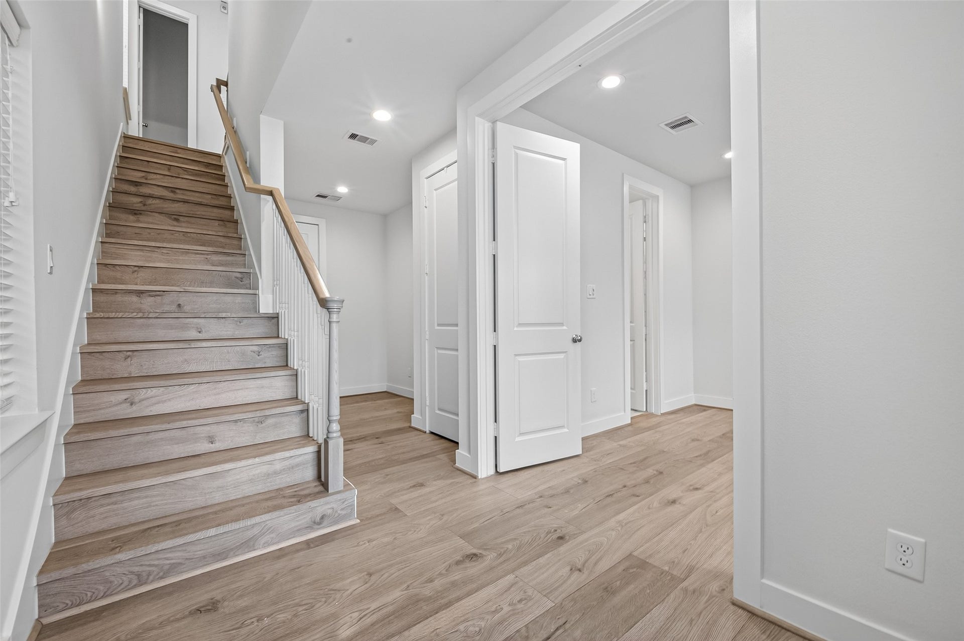 Bright and modern entryway featuring sleek Swiss floors, a stylish staircase with a wooden handrail, and crisp white walls leading to an inviting open space.