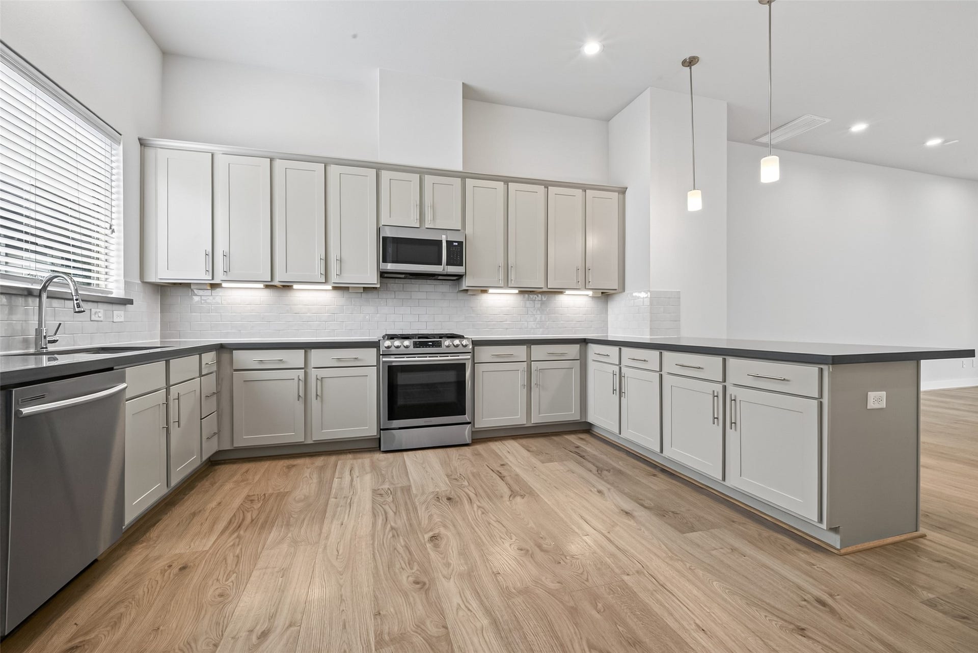 Spacious kitchen with sleek gray cabinetry, stainless steel appliances, and elegant pendant lighting, complemented by a large island and warm Swiss flooring.