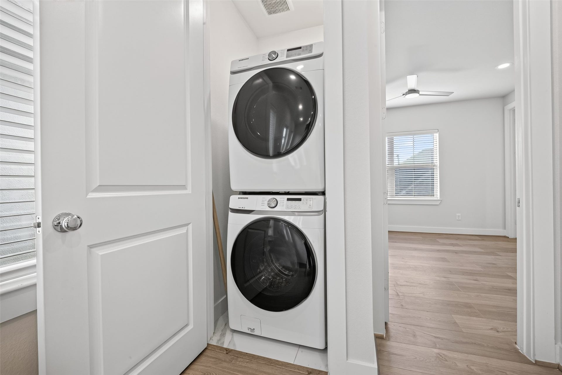 Convenient in-unit laundry area with a sleek, stacked washer and dryer set, adjacent to a bright room with modern Swiss flooring and natural light.