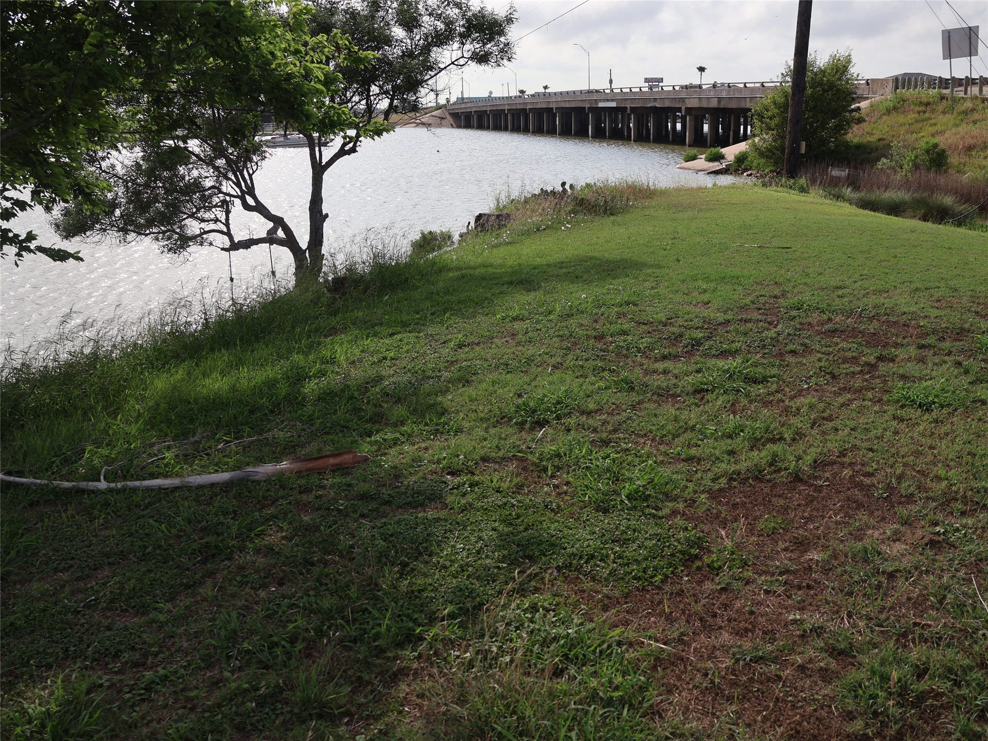 3401 Highway 6, Hitchcock, TX 77563 This photo shows a grassy area by a body of water, with a tree providing some shade. In the background, there's a bridge over the water, suggesting easy access to nearby areas. Ideal for those who enjoy waterfront views and outdoor space.