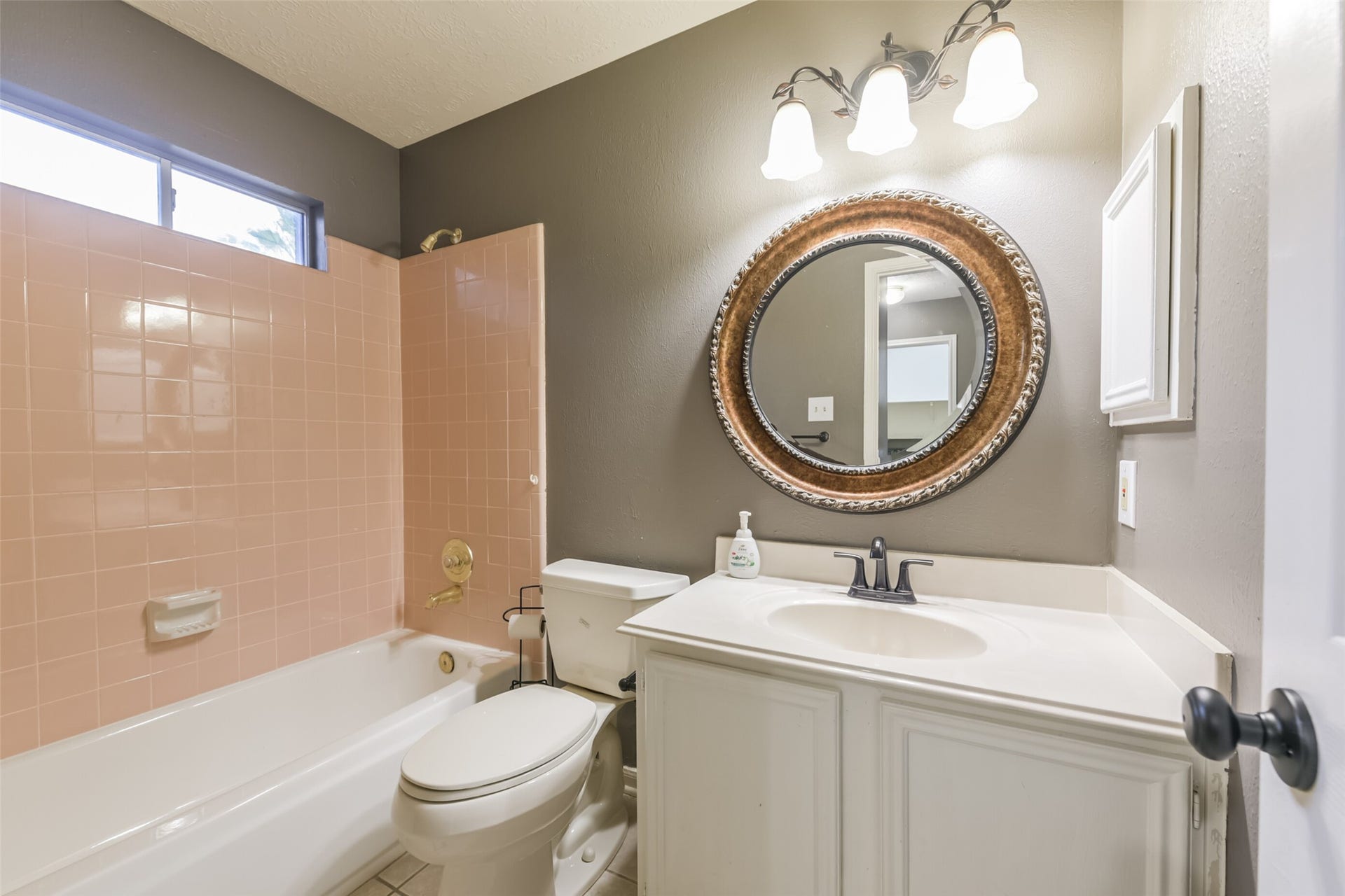 2509 S Mission Circle, Friendswood, TX 77546 Charming guest full bath with elegant lighting, a stylish round mirror, and classic pink tile accents.