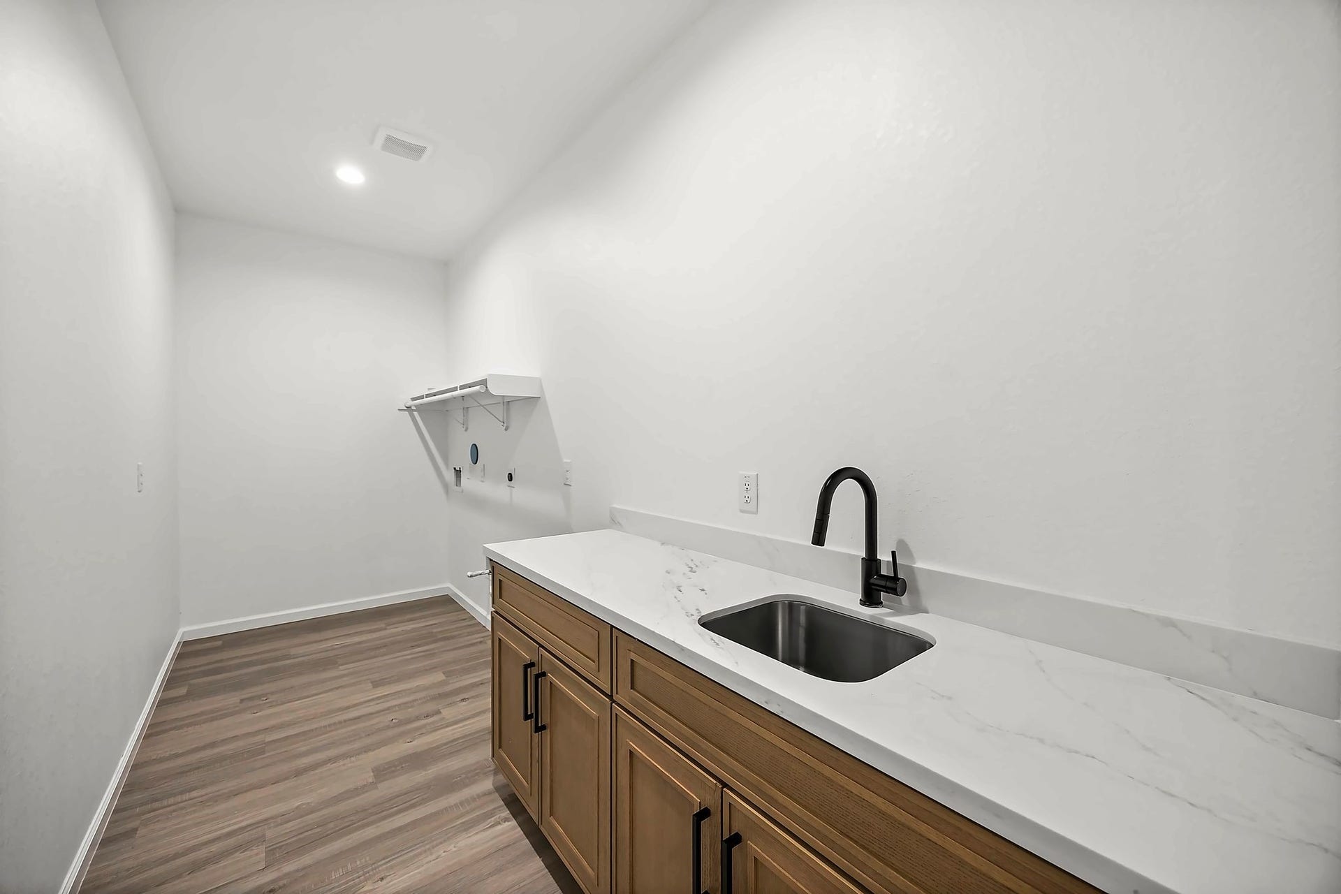 10426 Royal Oaks Drive, Houston, TX 77016 Spacious laundry room with elegant wood like flooring, modern cabinetry, and a sleek countertop featuring a built-in sink for convenience.
