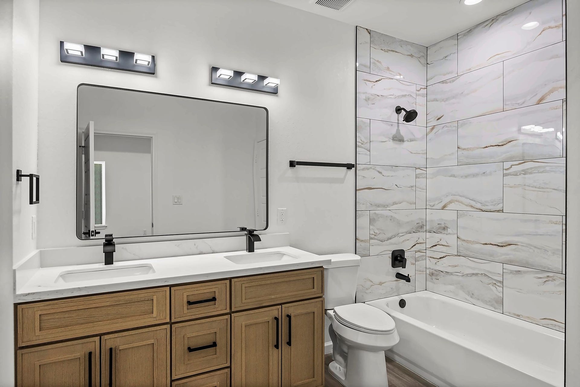 10426 Royal Oaks Drive, Houston, TX 77016 Modern bathroom featuring a sleek double vanity with dark fixtures, elegant marble-tiled shower, and warm wood cabinetry for a touch of luxury.