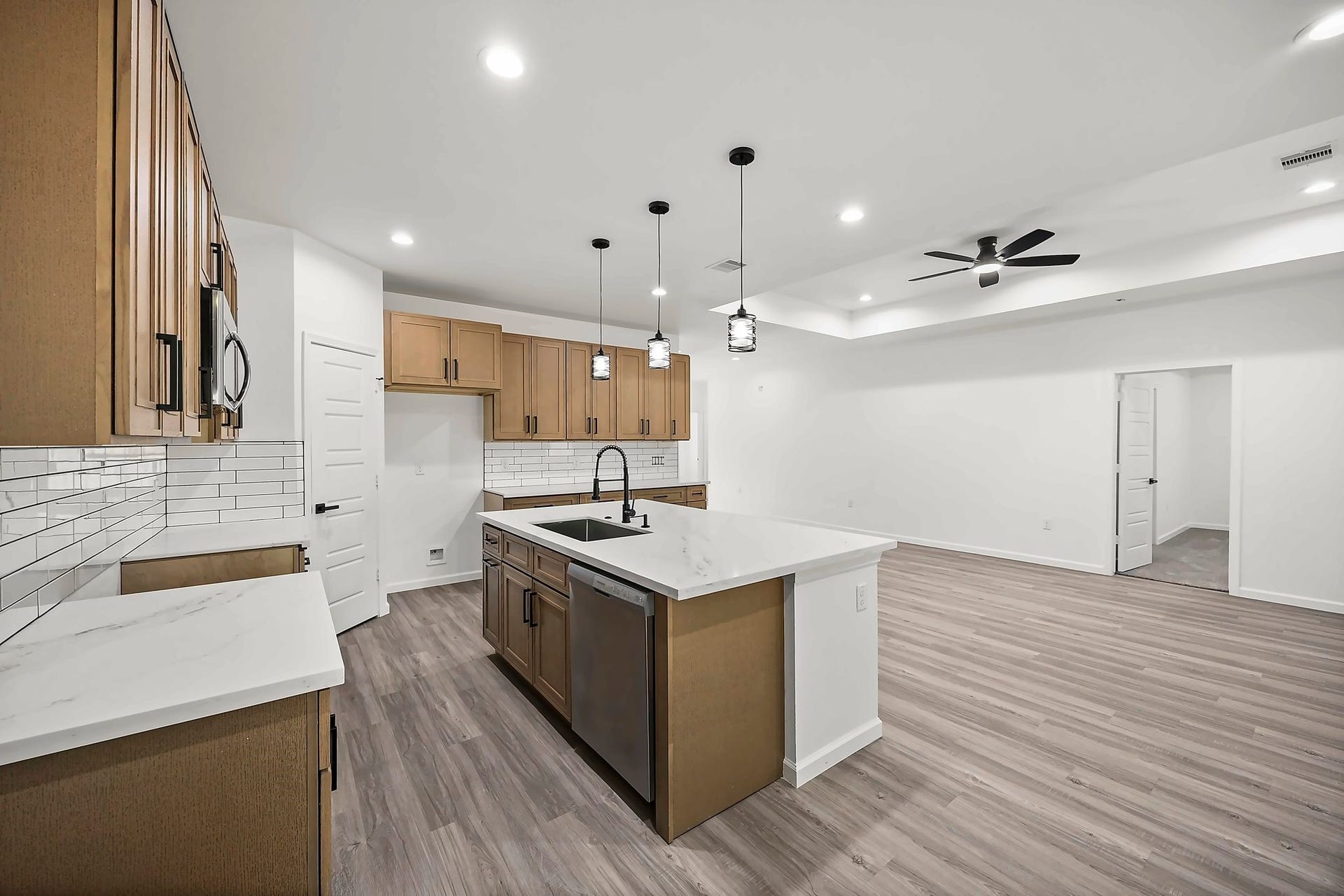 10426 Royal Oaks Drive, Houston, TX 77016 Modern open-concept kitchen with sleek wood cabinetry, a spacious island, and elegant pendant lighting, seamlessly connected to a bright living area with stylish wood like flooring and a ceiling fan.