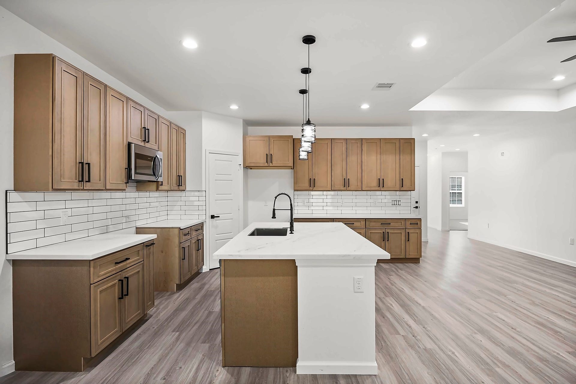 10426 Royal Oaks Drive, Houston, TX 77016 Spacious modern kitchen featuring sleek wood cabinetry, a large island with a sink, and elegant pendant lighting, complemented by a subway tile backsplash and stainless steel appliances.