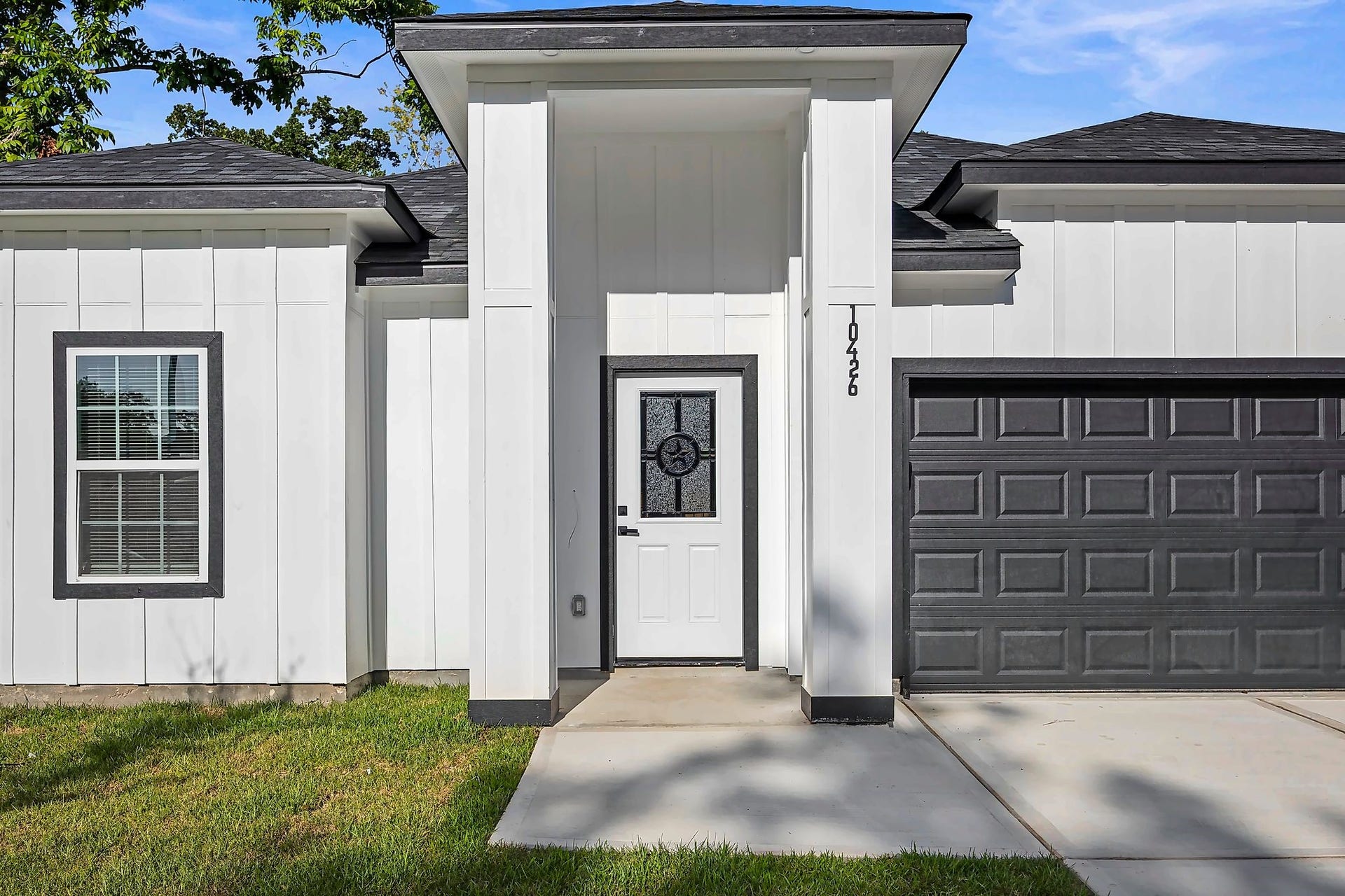10426 Royal Oaks Drive, Houston, TX 77016 Modern white facade with sleek black accents, featuring a stylish front door and attached garage, set against a well-maintained lawn.