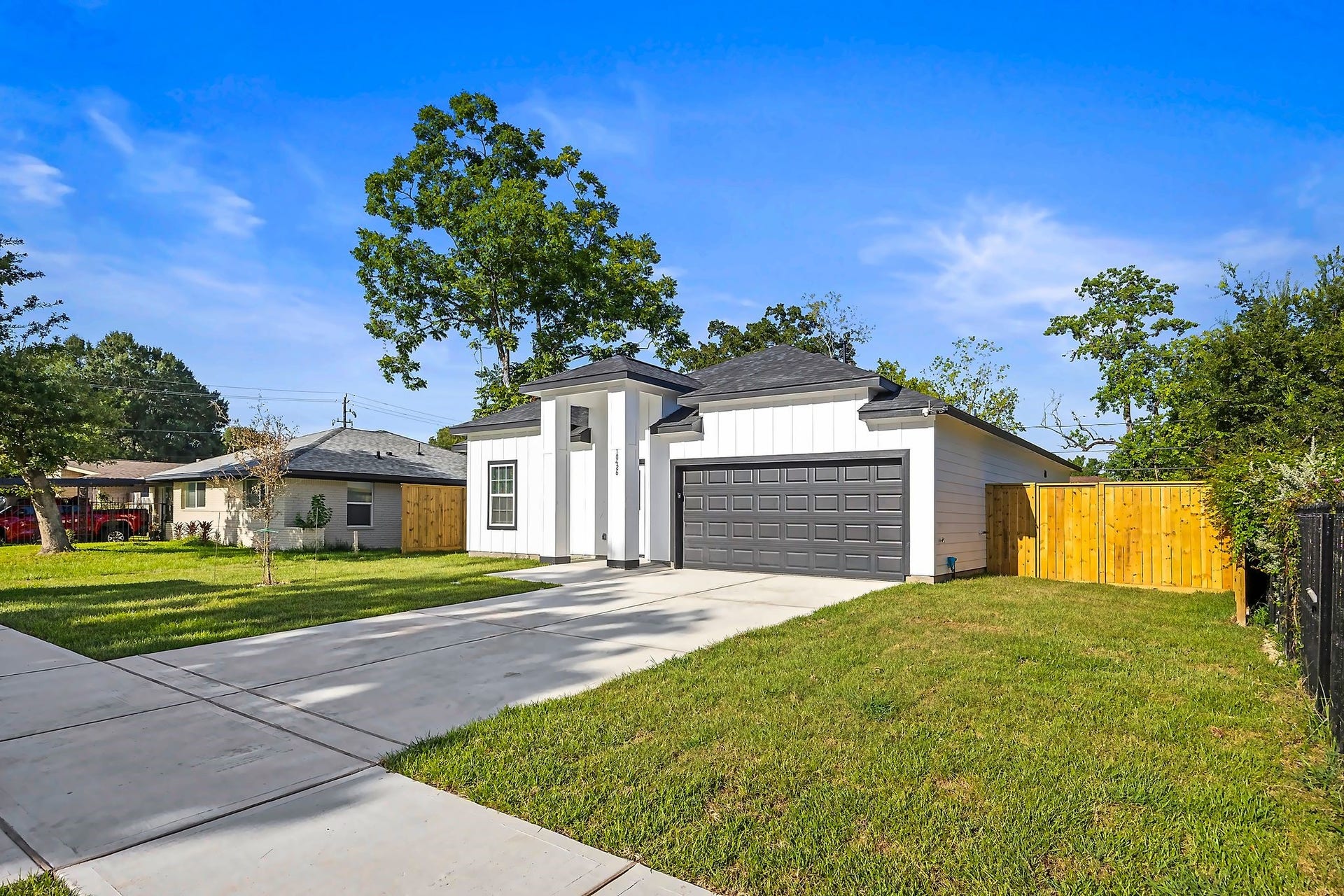 10426 Royal Oaks Drive, Houston, TX 77016 Modern single-story home with a sleek white exterior and contrasting dark garage door, set on a spacious, manicured lot with a wide driveway and fenced backyard.