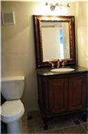 6001 Reims Road, #1202, Houston, TX 77036 This bathroom features a classic vanity with a dark countertop, an elegant framed mirror, and a toilet. The lighting is warm, enhancing the cozy feel.