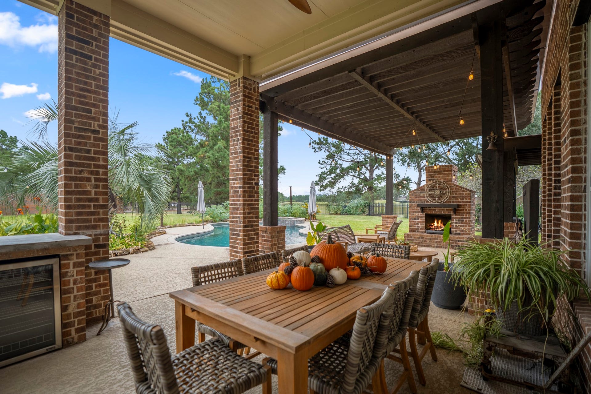 Enjoy year-round outdoor living with covered patio featuring brick columns, ceiling fan, and outdoor kitchenette complete with a built-in beverage refrigerator.
