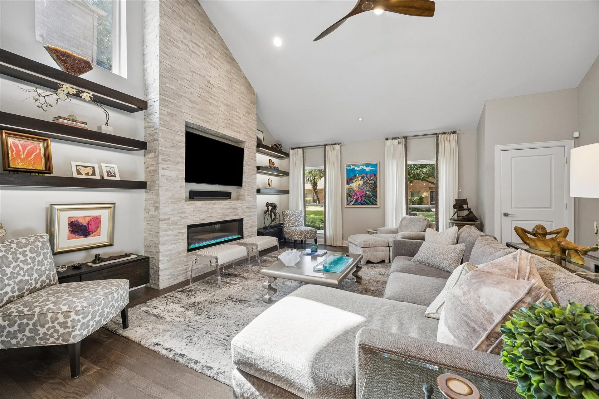 LIVING ROOM: Light-filled living room showcases soaring ceilings, a dramatic fireplace with remote, programmable heat/colors, stacked stone surround and custom floating shelves.