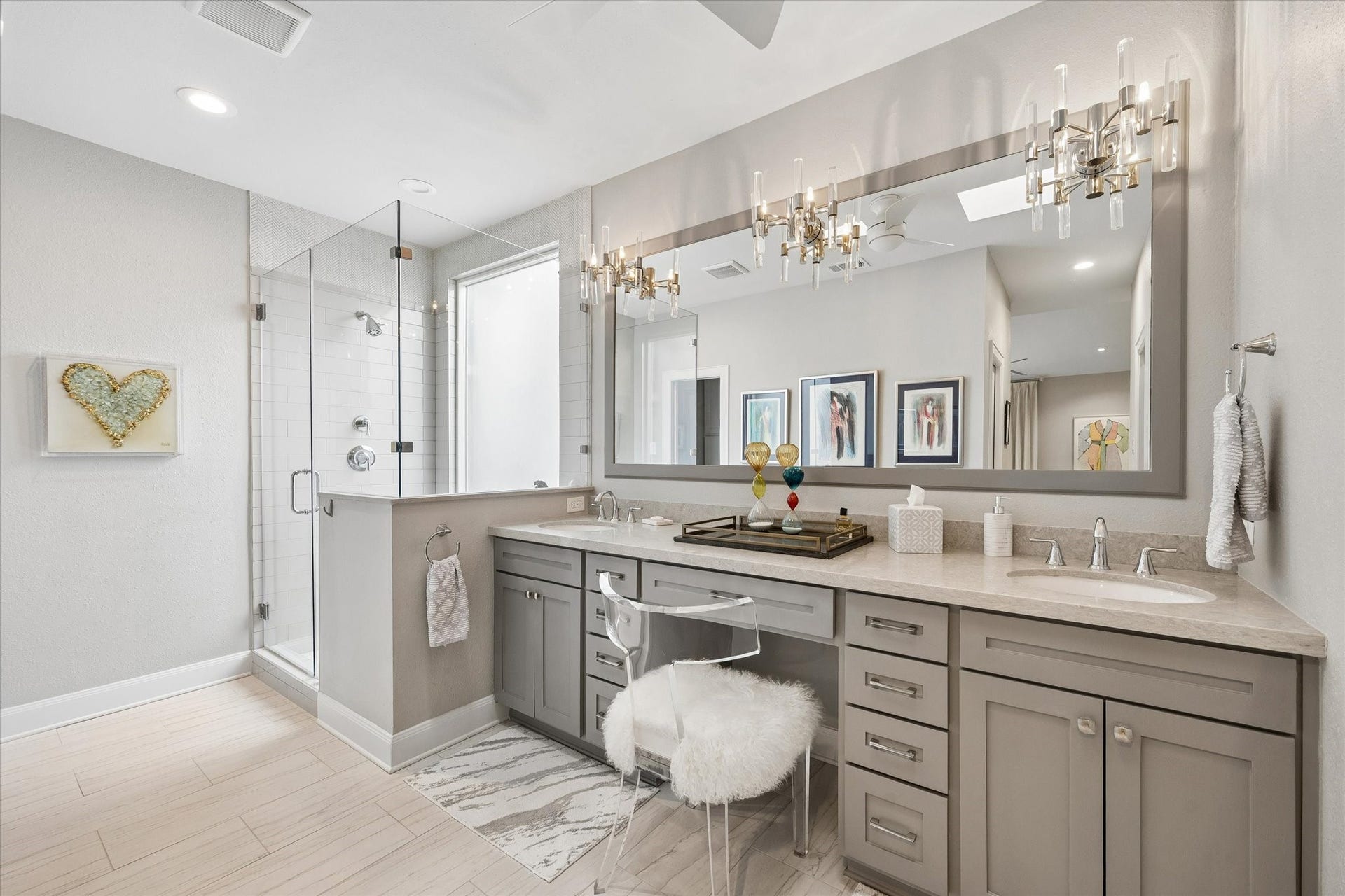 PRIMARY BATHROOM: Beautifully renovated and redesigned primary bathroom showcases dual vanities with marble countertops, custom cabinetry, elegant lighting and a glass-enclosed walk-in shower with body sprayer.