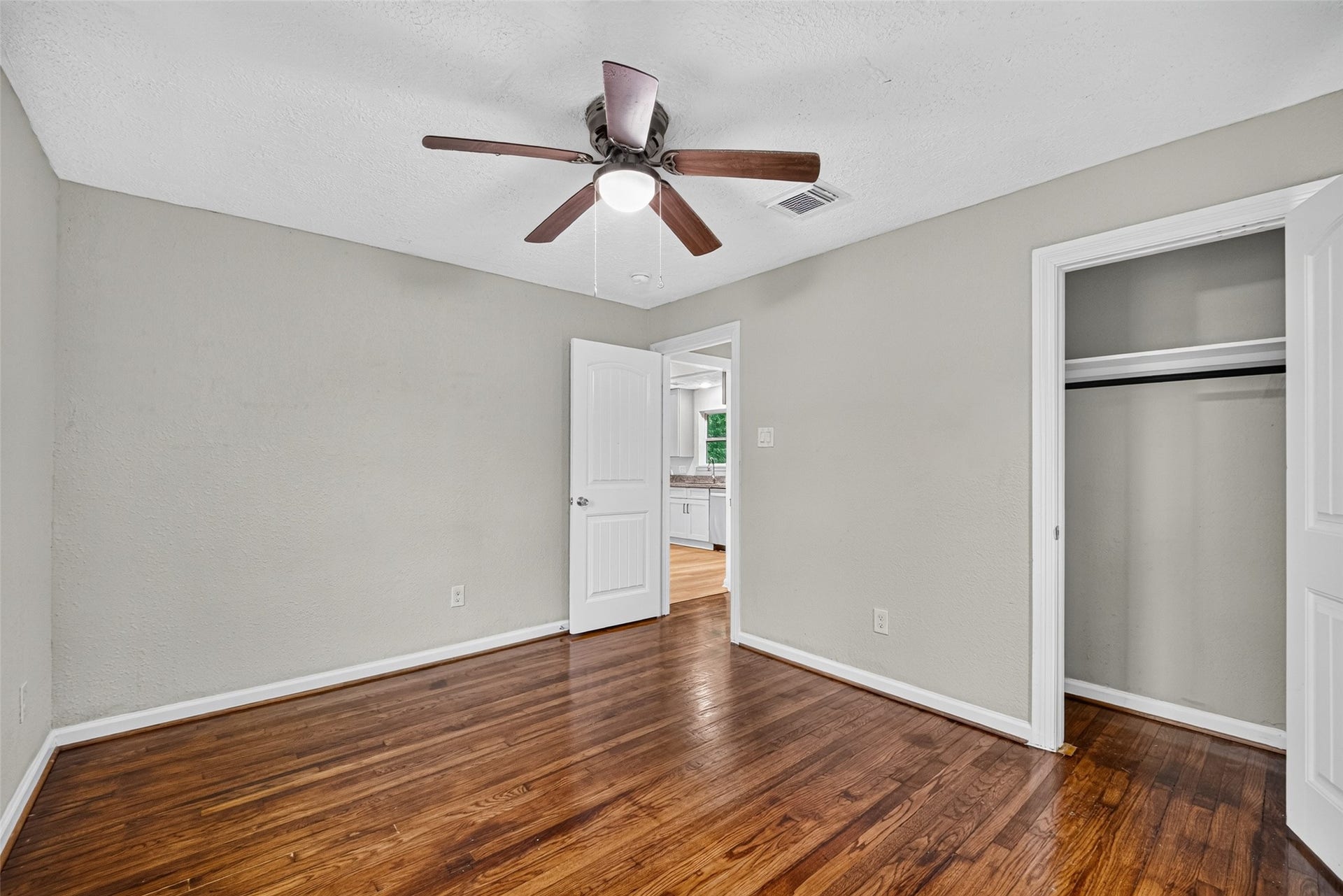 Bedroom 1 with ceiling fan and refinished original wood flooring.