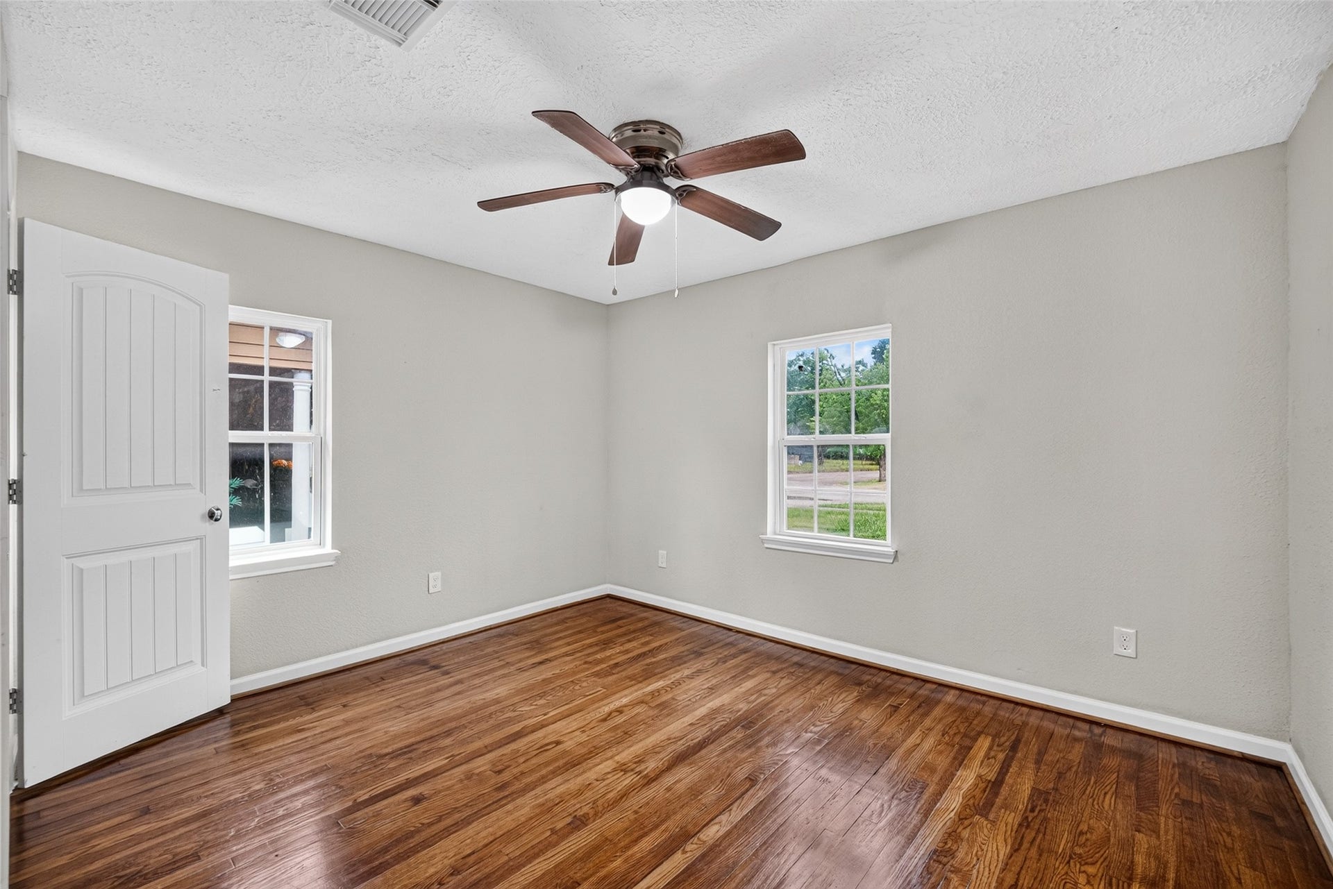 Bedroom 1 with ceiling fan and refinished original wood flooring.