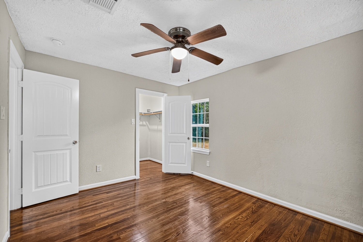 Bedroom 2 with ceiling fan and refinished original wood flooring.
