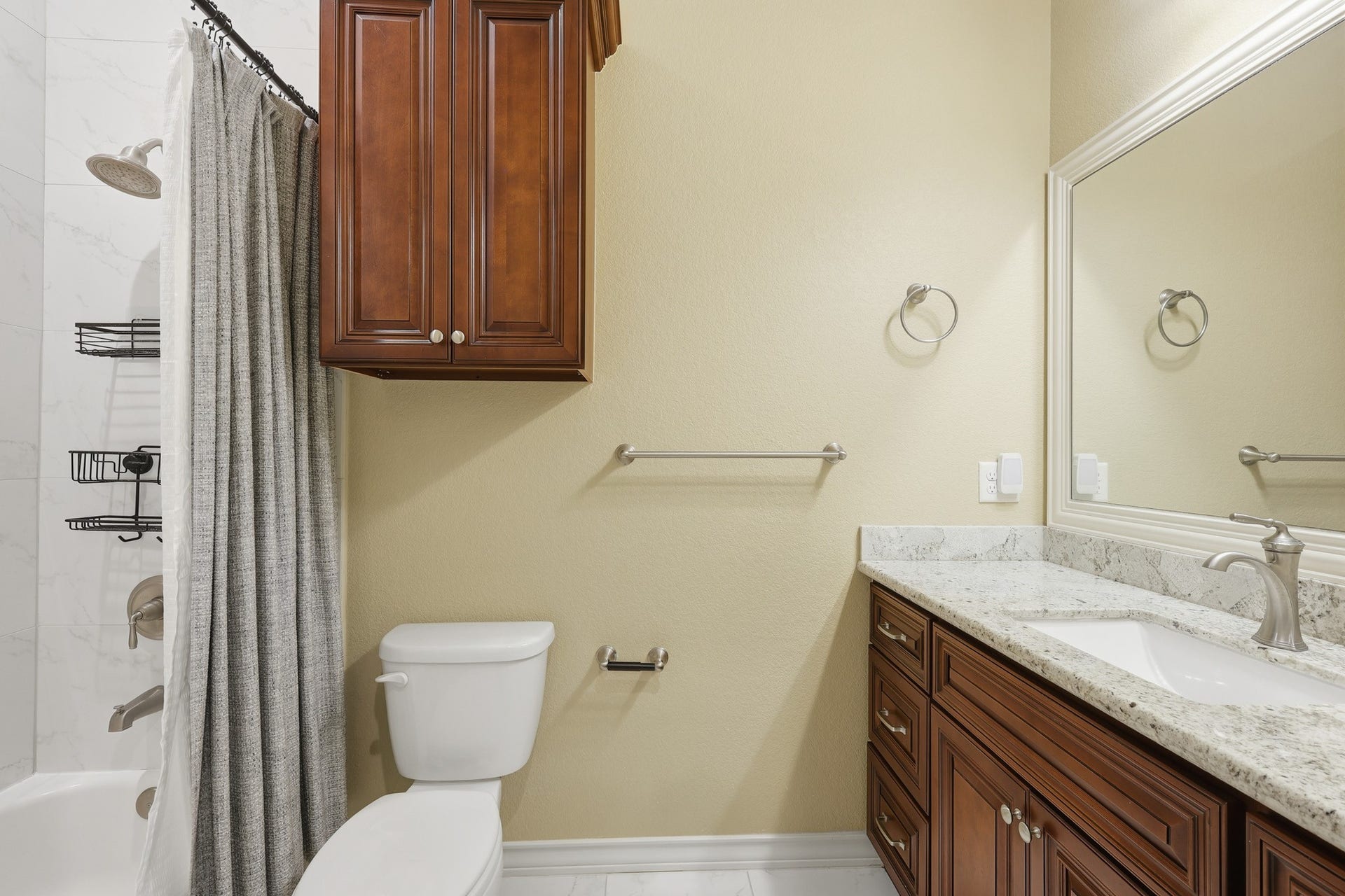 The secondary en suite bath features custom cherry wood cabinetry, granite countertops, and marble-inspired tile surrounding the tub and shower, delivering a timeless and refined aesthetic.