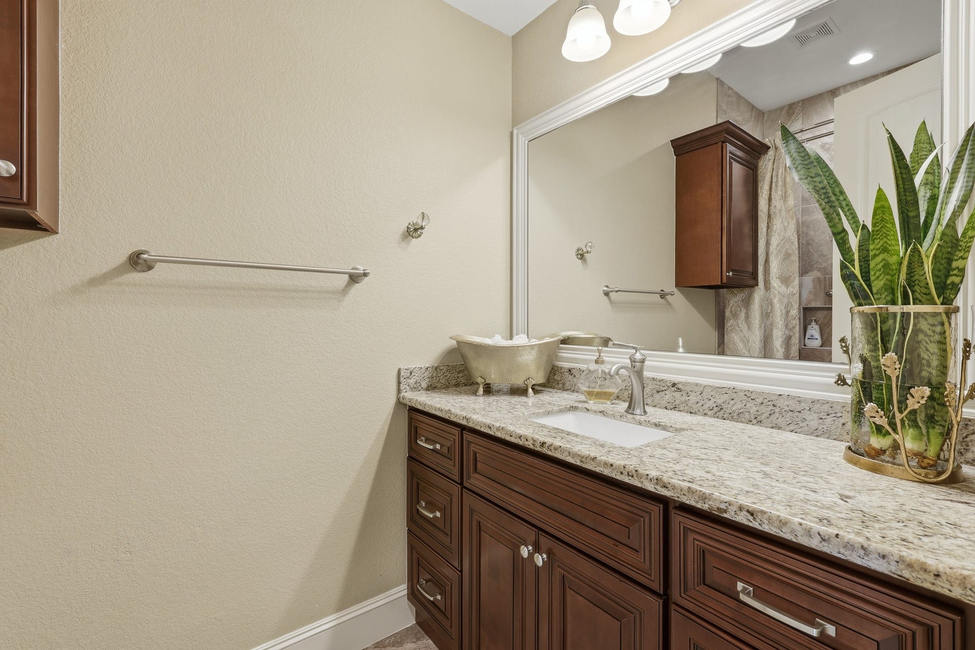 First-floor full bath offers both comfort and style. Rich cherry cabinetry is paired with granite countertops and a framed mirror, creating a warm and sophisticated aesthetic. The spacious walk-in shower features floor-to-ceiling tile, decorative accent detailing, and a pebble-style shower floor for a refined, spa-inspired feel. Well-placed lighting and quality finishes throughout complete this beautifully maintained bath, ideal for guests or convenient main-level living.