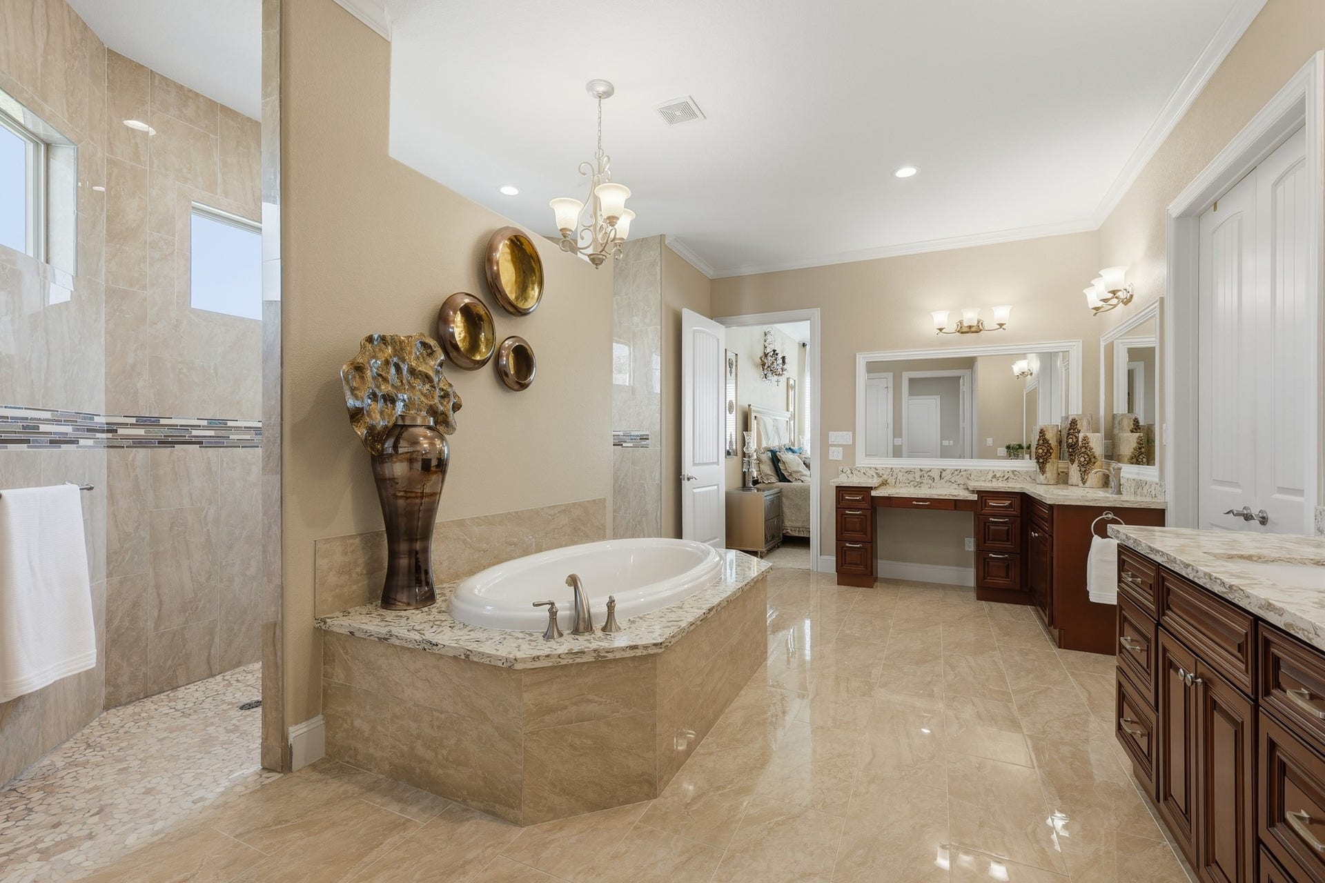 Indulge in spa-inspired luxury within this expansive primary bathroom. A stunning soaking tub is framed by rich stone surrounds, creating a serene focal point, while the oversized walk-in shower features full-height tile, decorative accent detailing, and natural light for a bright, refreshing experience.