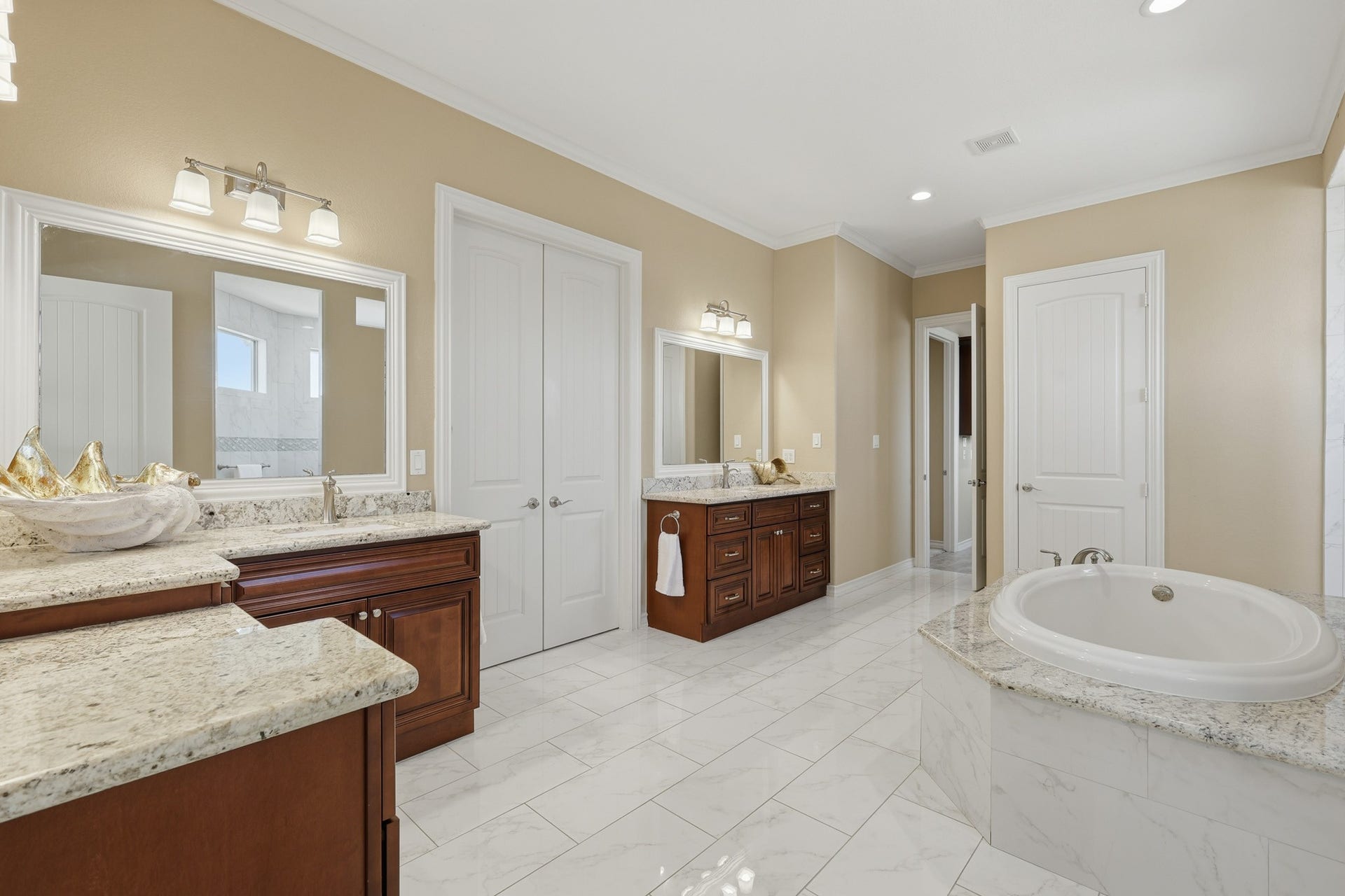 This impressive second-floor primary bathroom offers a spa-inspired retreat with an oversized soaking tub framed in elegant marble-look tile, dual vanities with custom cherry wood cabinetry, and expansive granite countertops. The spacious layout and refined finishes create an atmosphere of elevated comfort and luxury.