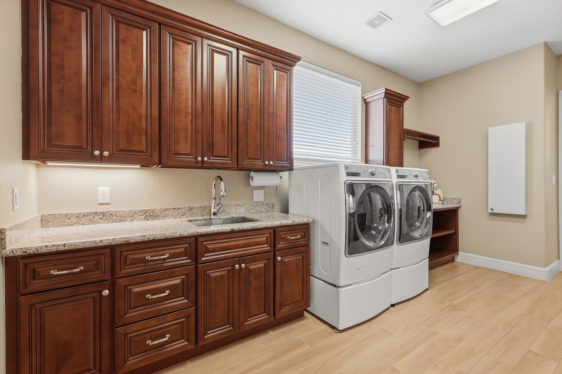 Conveniently located just off the primary suite and garage, this beautifully appointed first-floor utility room combines functionality with refined design. Custom cherry cabinetry provides abundant storage, complemented by granite countertops and a built-in utility sink for added convenience. Thoughtfully designed with generous workspace and organization in mind, this well-equipped laundry area elevates everyday tasks with both style and efficiency.