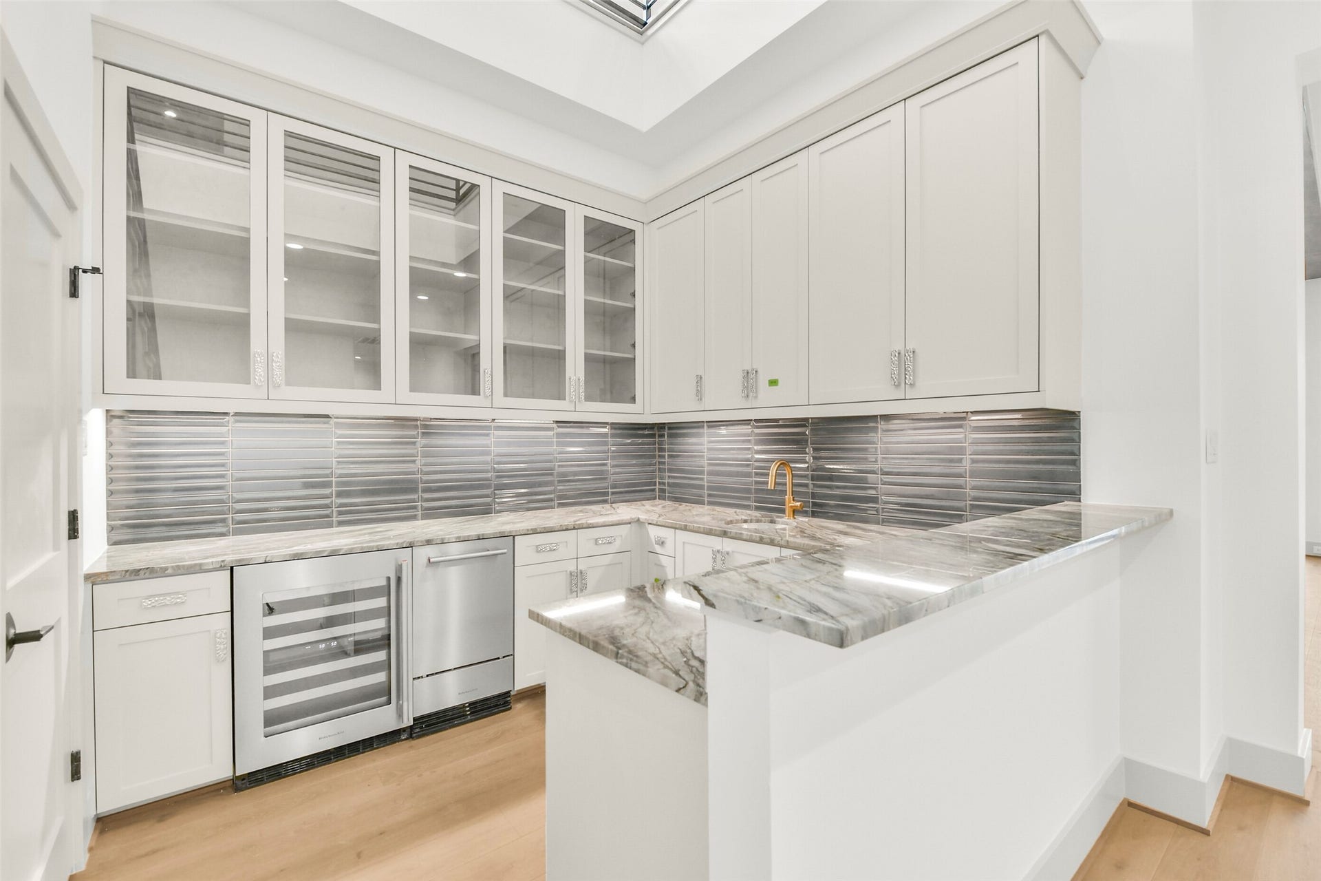 This view of the wet bar shows the Kitchenaid 46 bottle capacity wine refrigerator, 35lb capacity ice maker, glass front cabinets and brass finished sink and faucet.