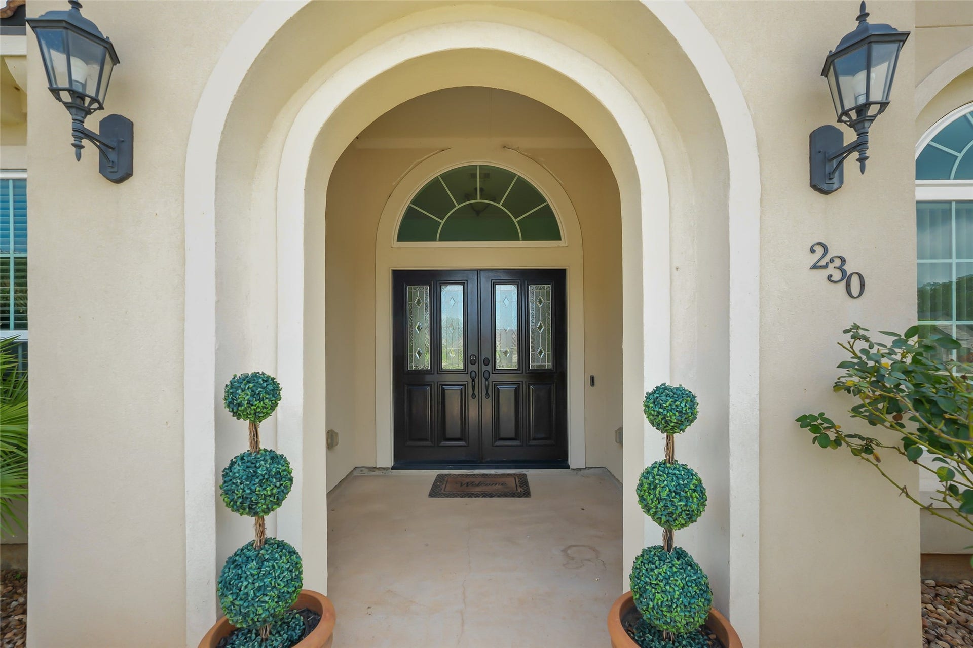 230 Lawrence Marshall Drive, Hempstead, TX 77445 Covered front entry featuring an arched doorway, elegant double front doors, and timeless architectural details.