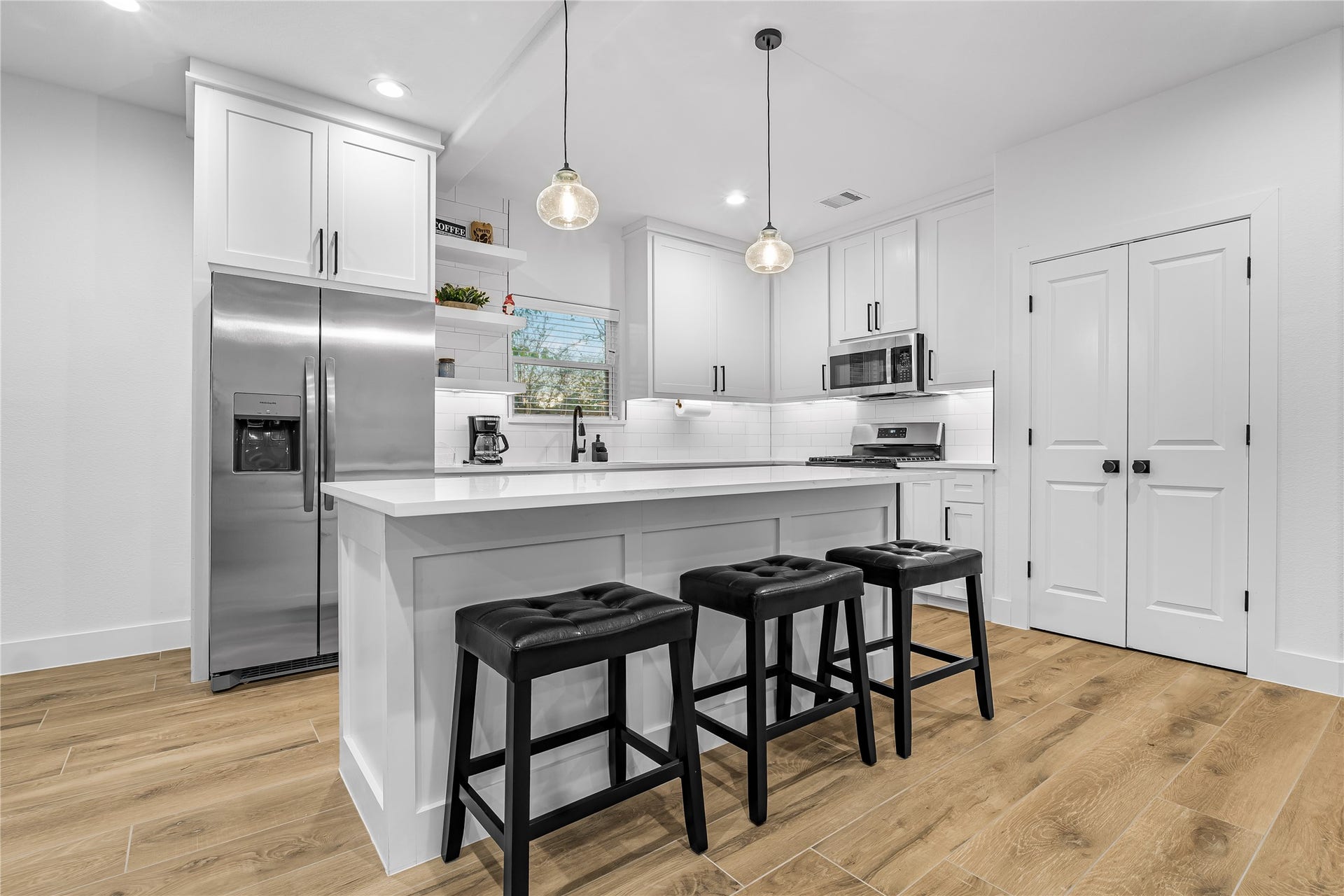 7107 Foster Street, #B, Houston, TX 77021 Bright and modern kitchen features sleek white cabinetry, a spacious island with seating, stainless steel appliances, and stylish pendant lighting. Actual furniture.