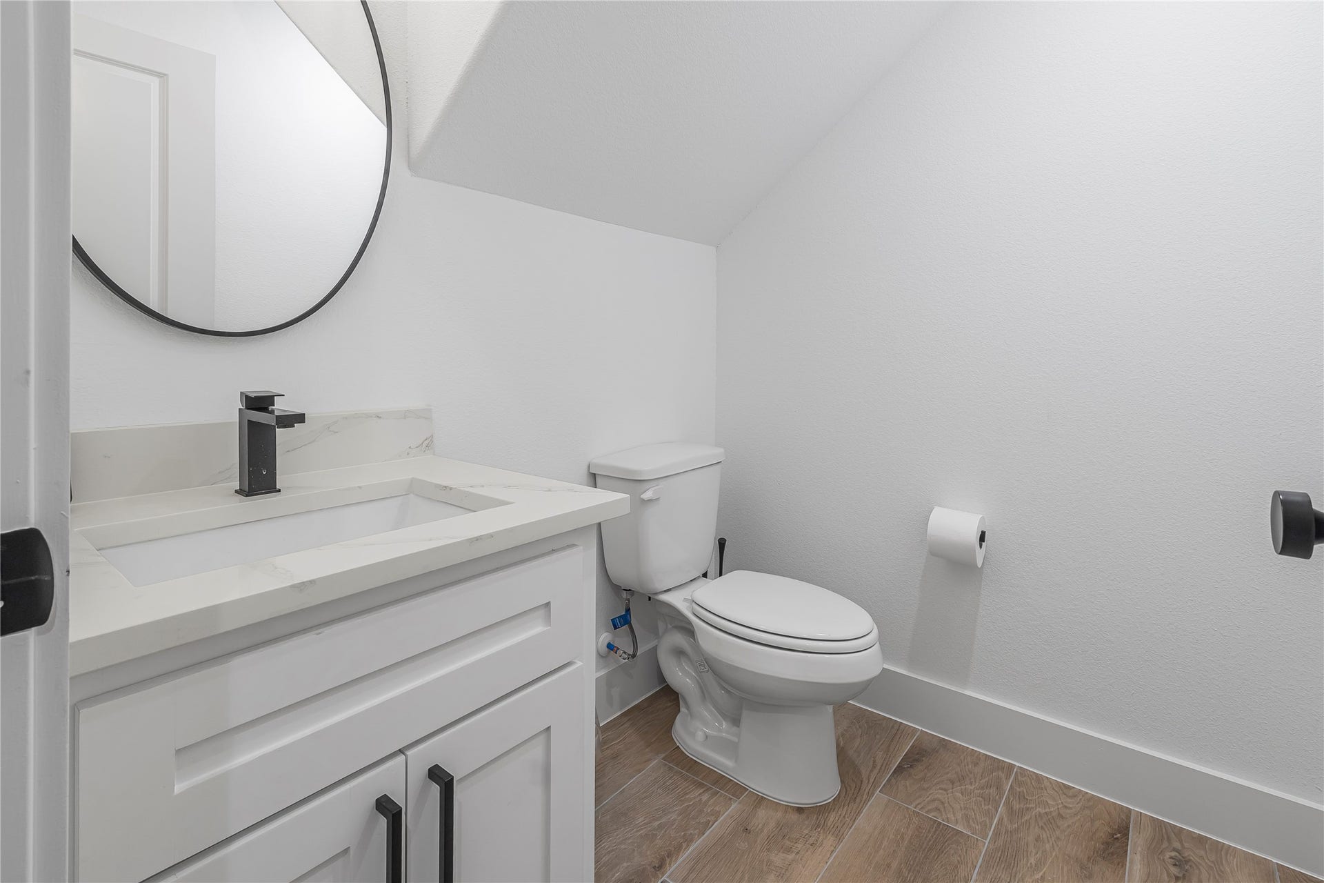 7107 Foster Street, #B, Houston, TX 77021 Chic powder room featuring a sleek white vanity with a quartz countertop, modern black fixtures, and warm wood-look flooring.