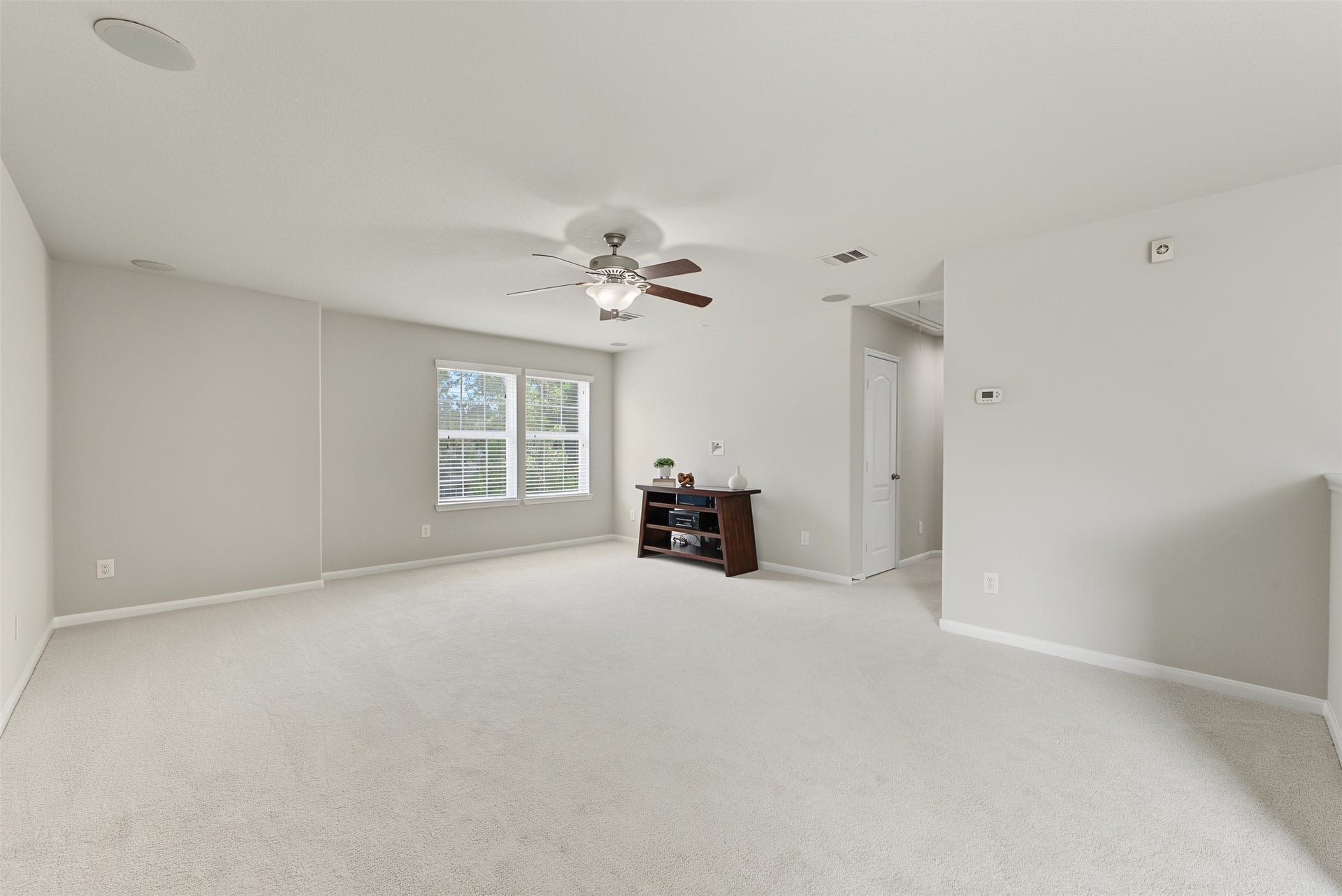 Spacious and bright gameroom featuring new carpeting, neutral walls, and a ceiling fan, with ample natural light from large windows. Perfect for relaxation or entertaining.
