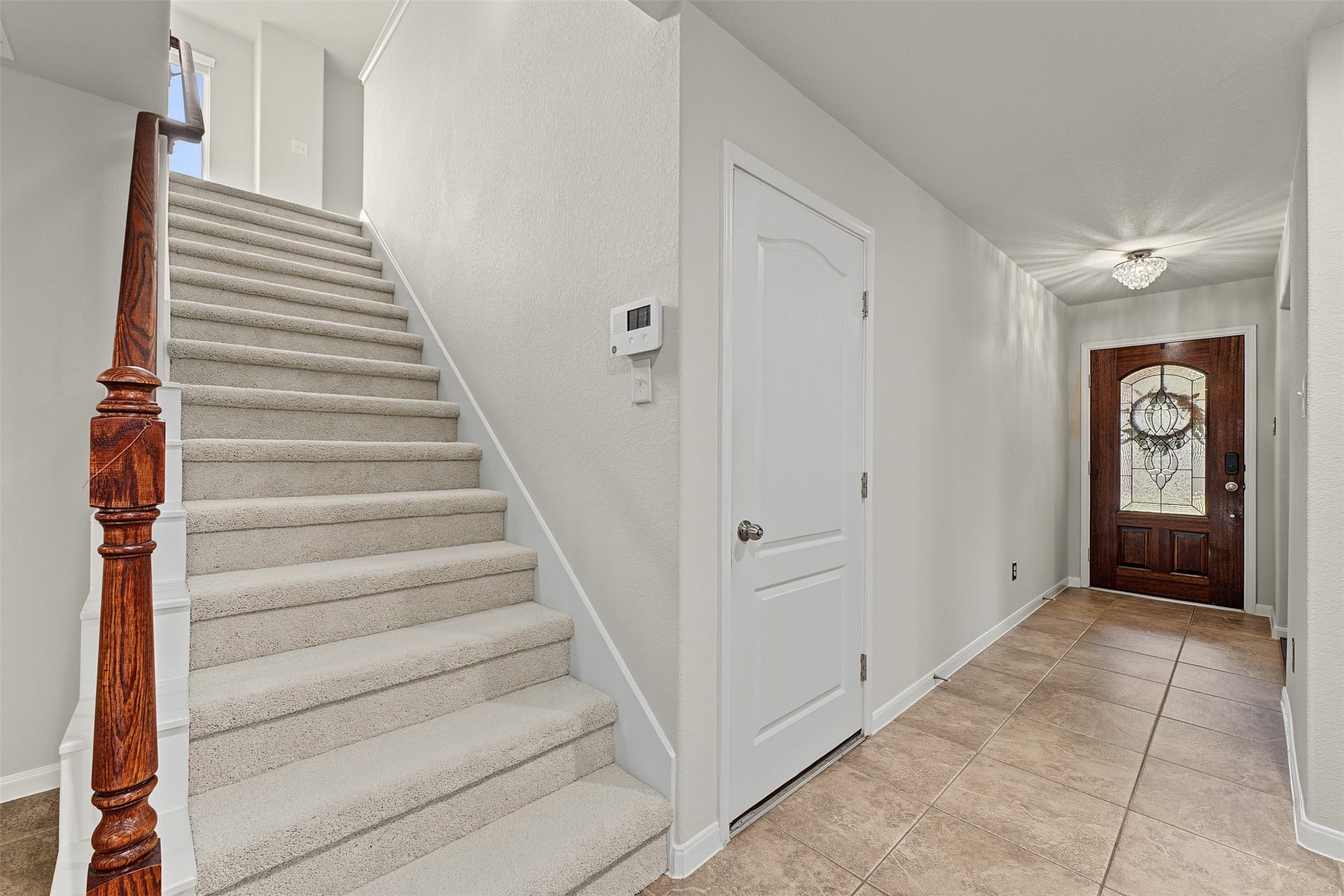 Inviting entryway features a beautifully crafted wooden front door, elegant tile flooring, and a carpeted staircase with a polished wooden railing leading to the upper level.