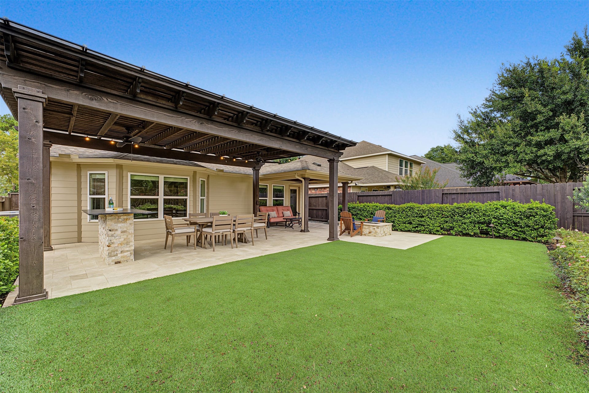 Charming backyard oasis featuring a spacious pergola-covered patio with ample seating, a built-in bar area, and low maintenance turf, perfect for outdoor entertaining.