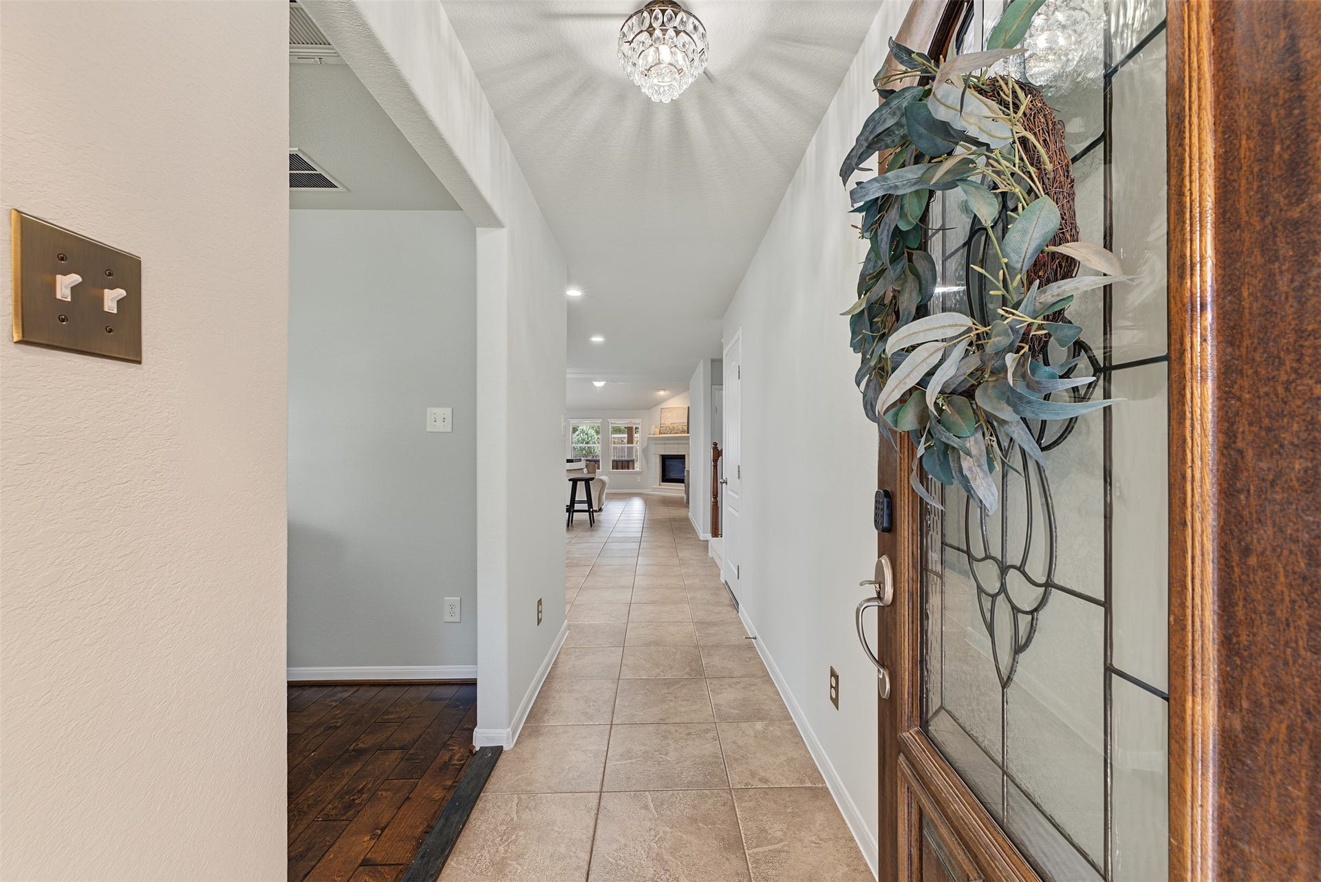 Inviting entryway with elegant tile flooring leads to a bright, open living space, enhanced by a decorative glass front door and charming overhead lighting.