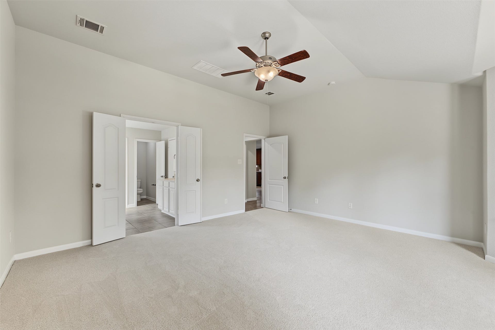Spacious bedroom with plush new carpeting, a ceiling fan, and direct access to a bright en-suite bathroom through double doors.