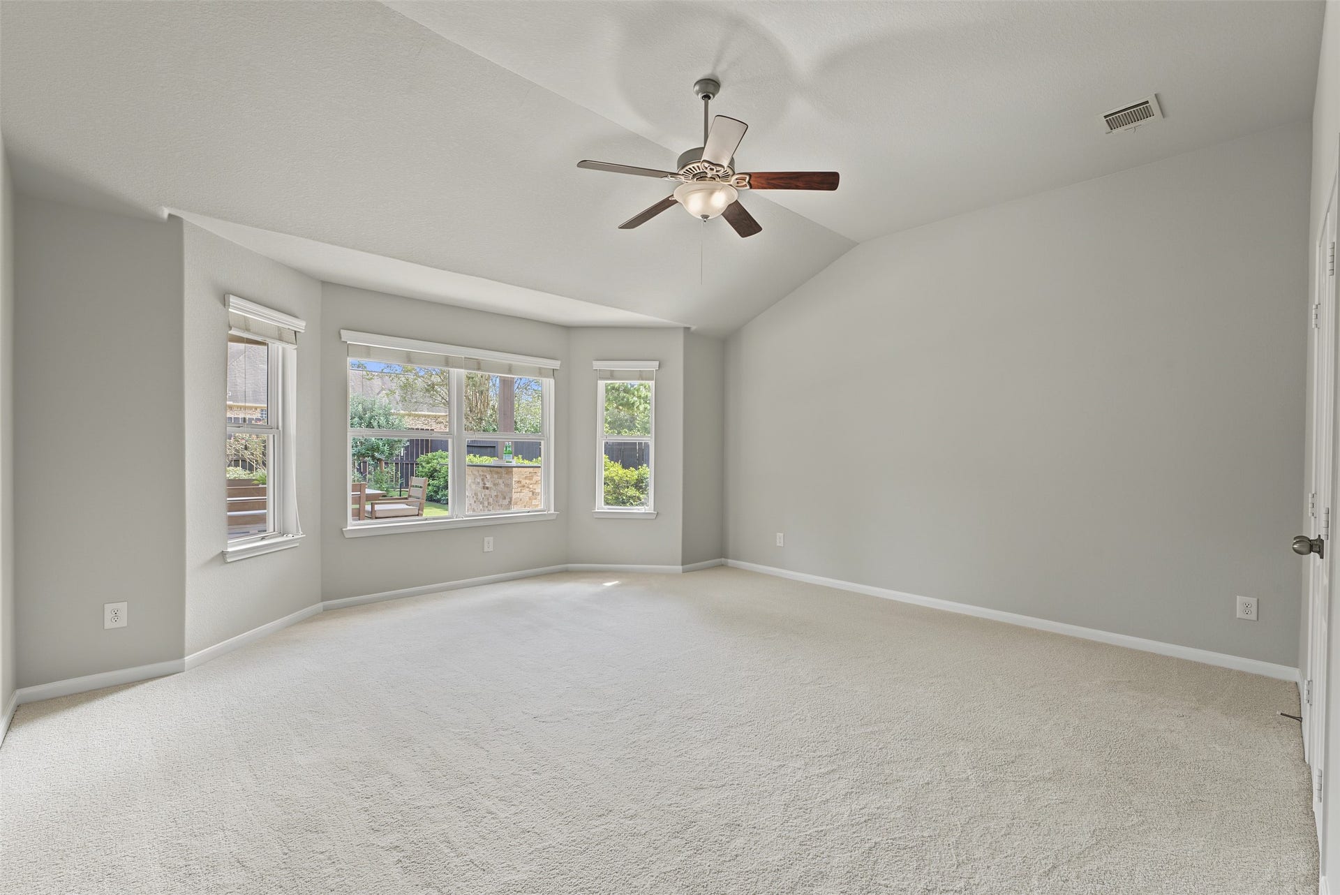 Spacious primary bedroom with vaulted ceilings, a ceiling fan, and large windows offering abundant natural light and views of the landscaped backyard.